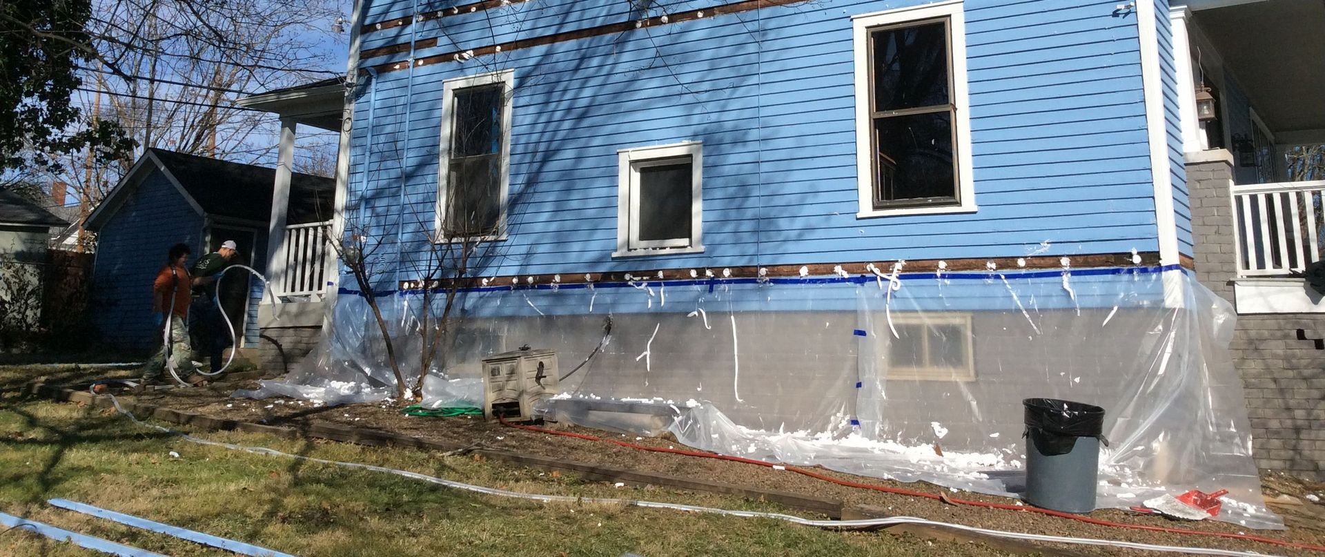 A blue house is being remodeled and covered in plastic.