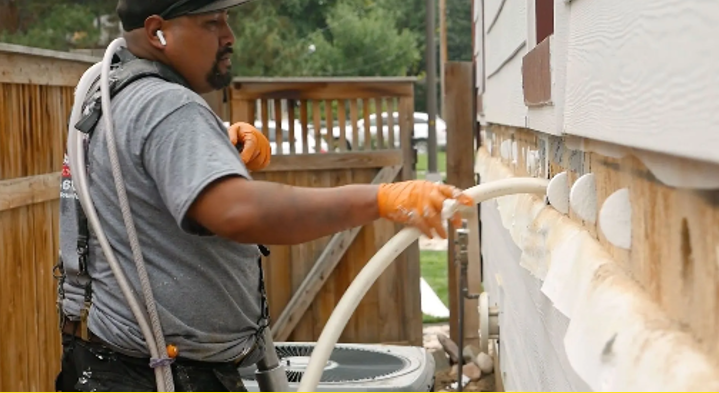 A man is working on the side of a house with a hose.