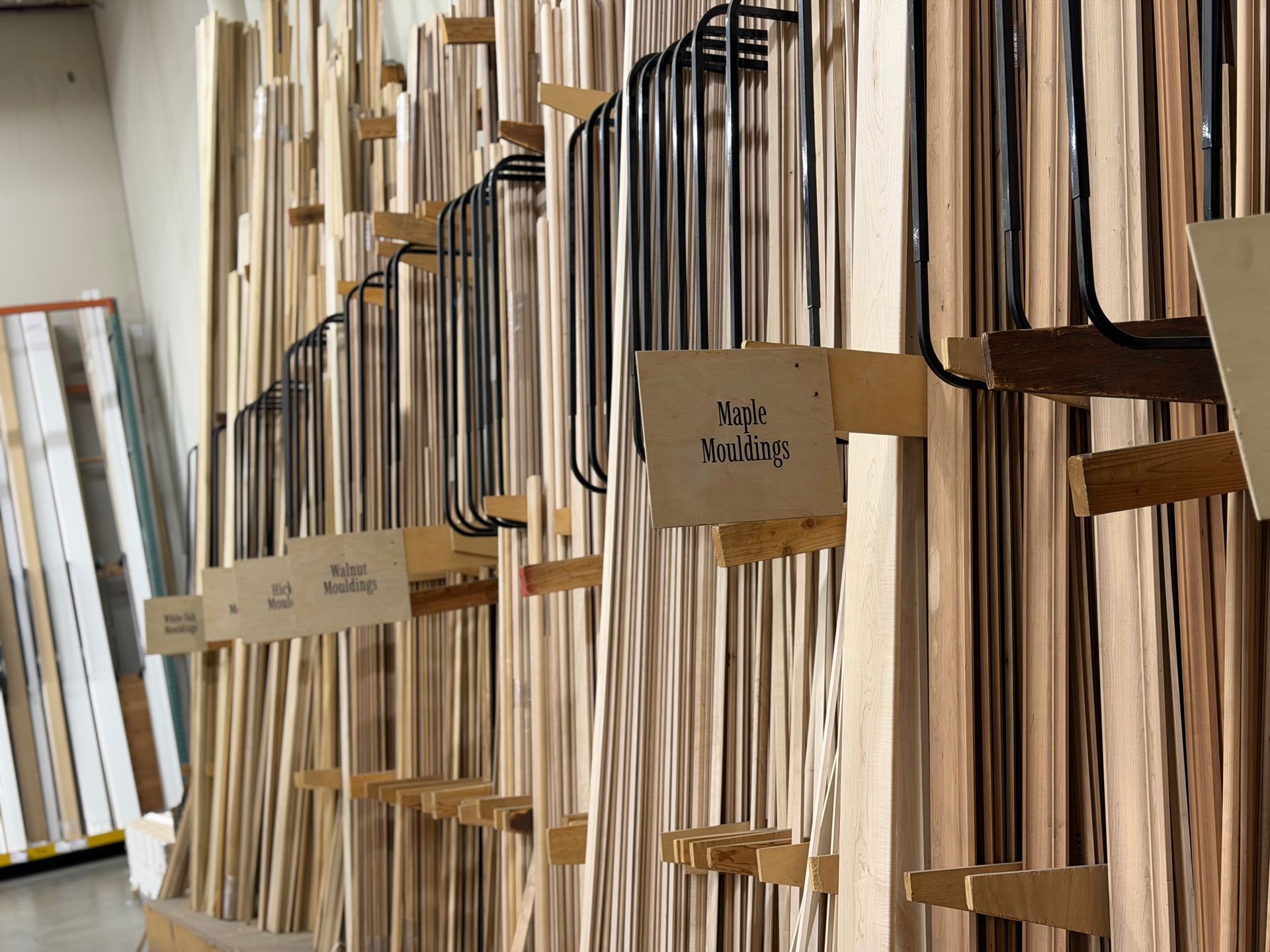 Shelves filled with various wooden boards in a lumberyard, with labels for different types of wood.