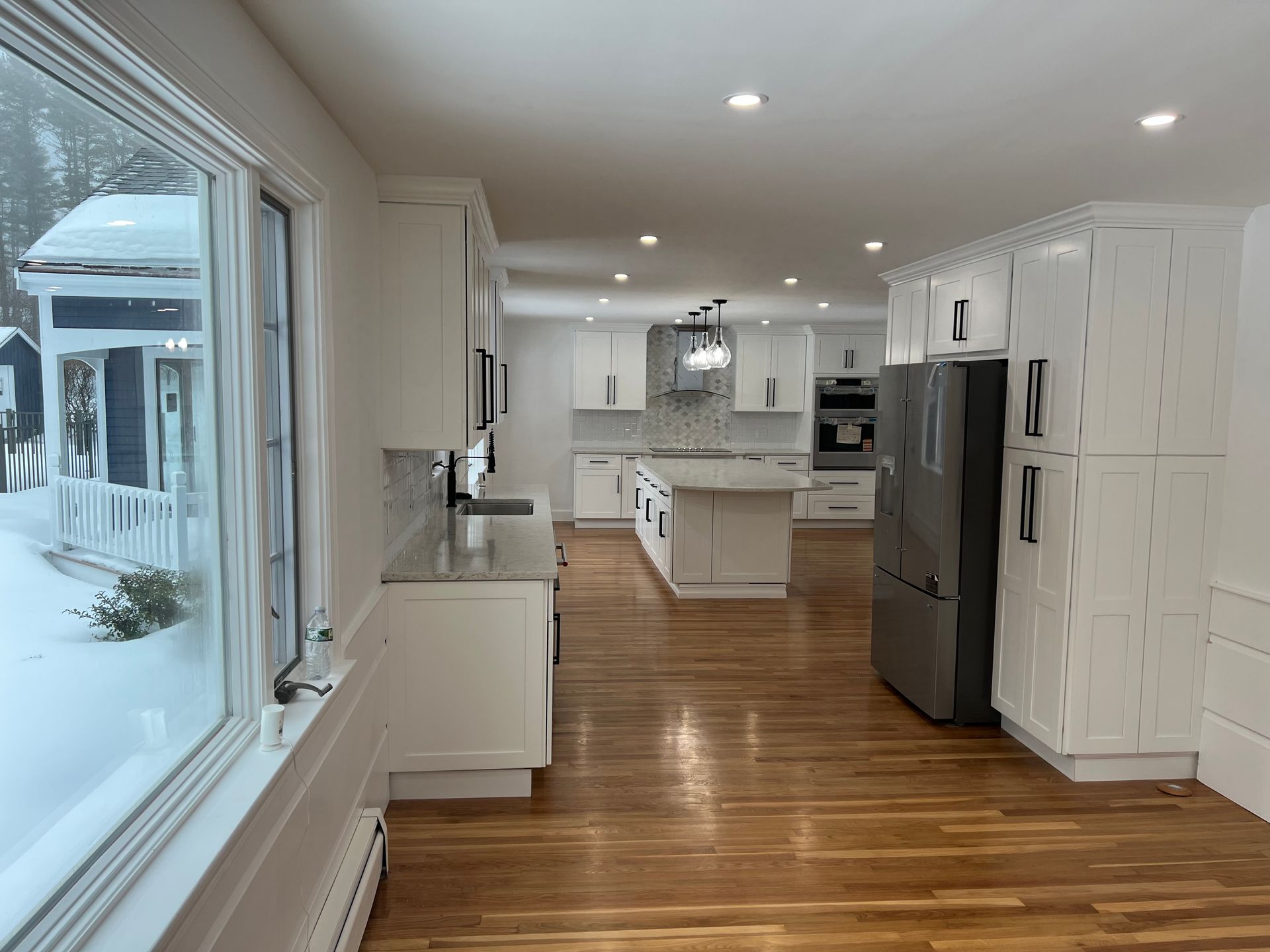 A bright, modern kitchen featuring white cabinets, stainless steel appliances, a center island, and wood flooring.