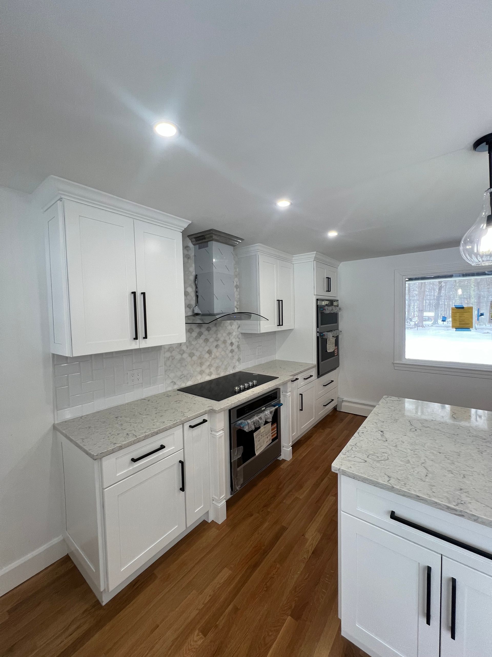A modern kitchen featuring white cabinets, speckled granite countertops, stainless steel appliances, and wood flooring.