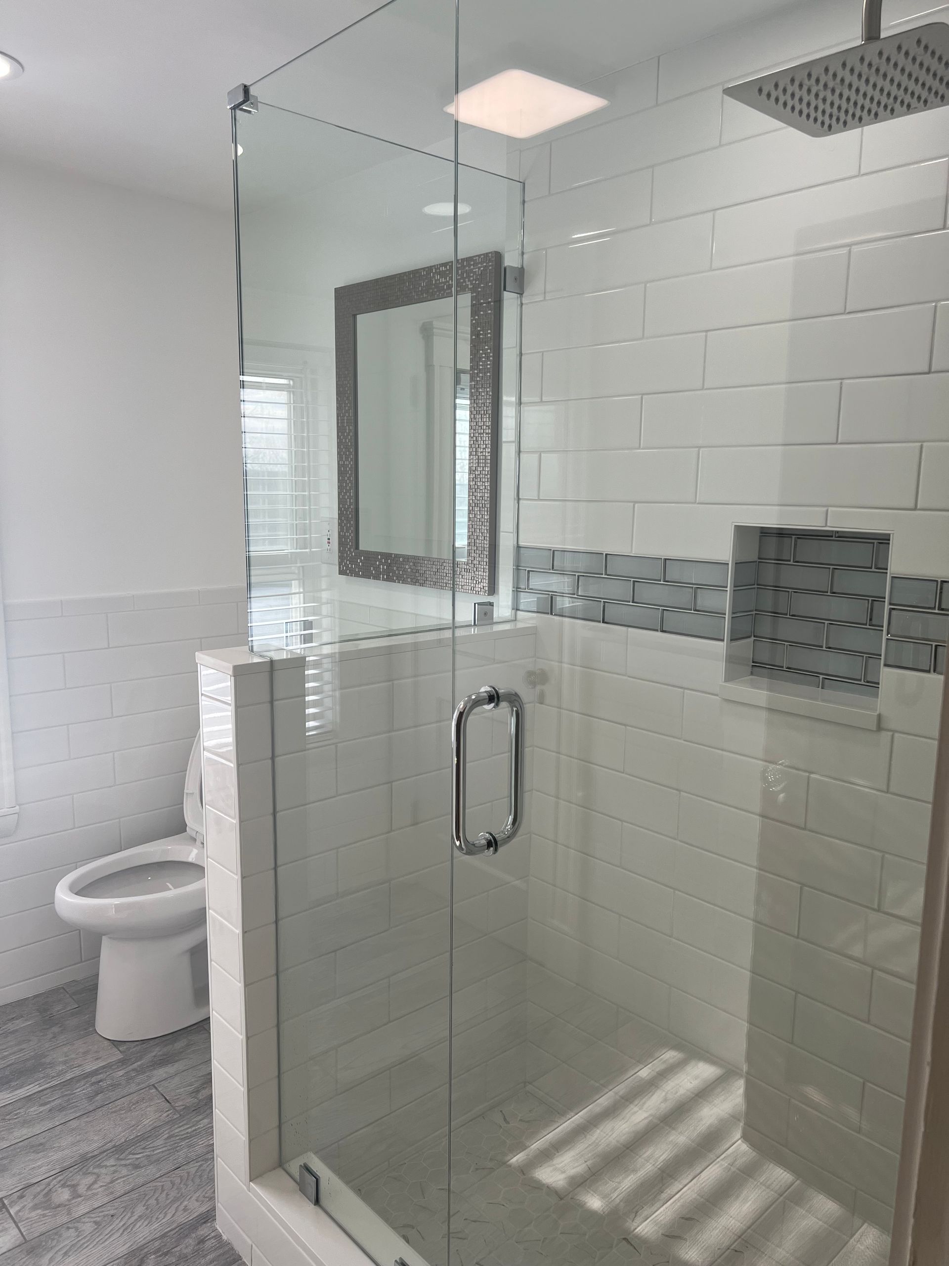 A bathroom with a walk in shower , toilet and mirror.