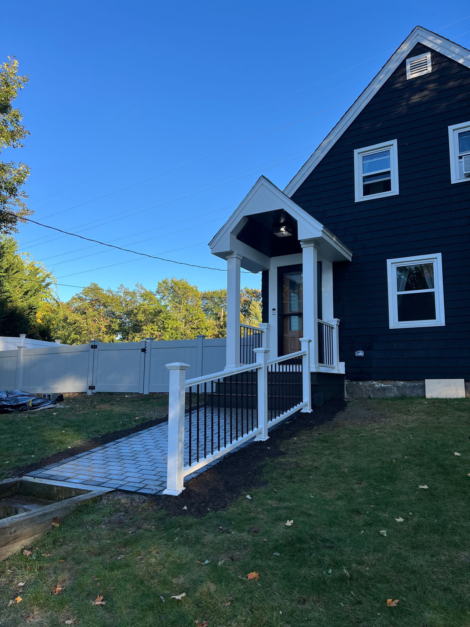 Dark blue house with white porch and ramp, black railings, clear sky