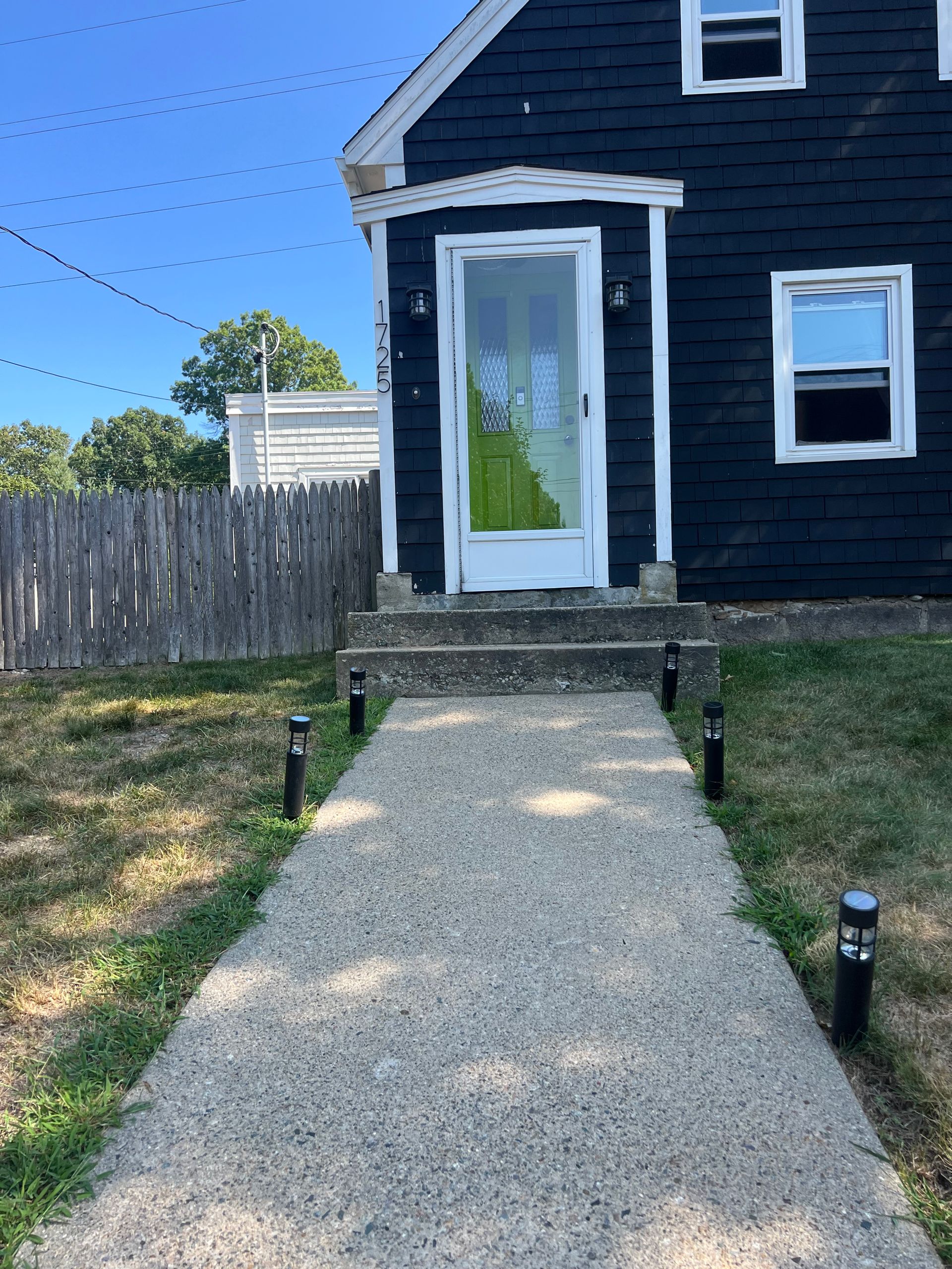 A dark-painted house with a concrete walkway leading to the front door, lined with small black lights