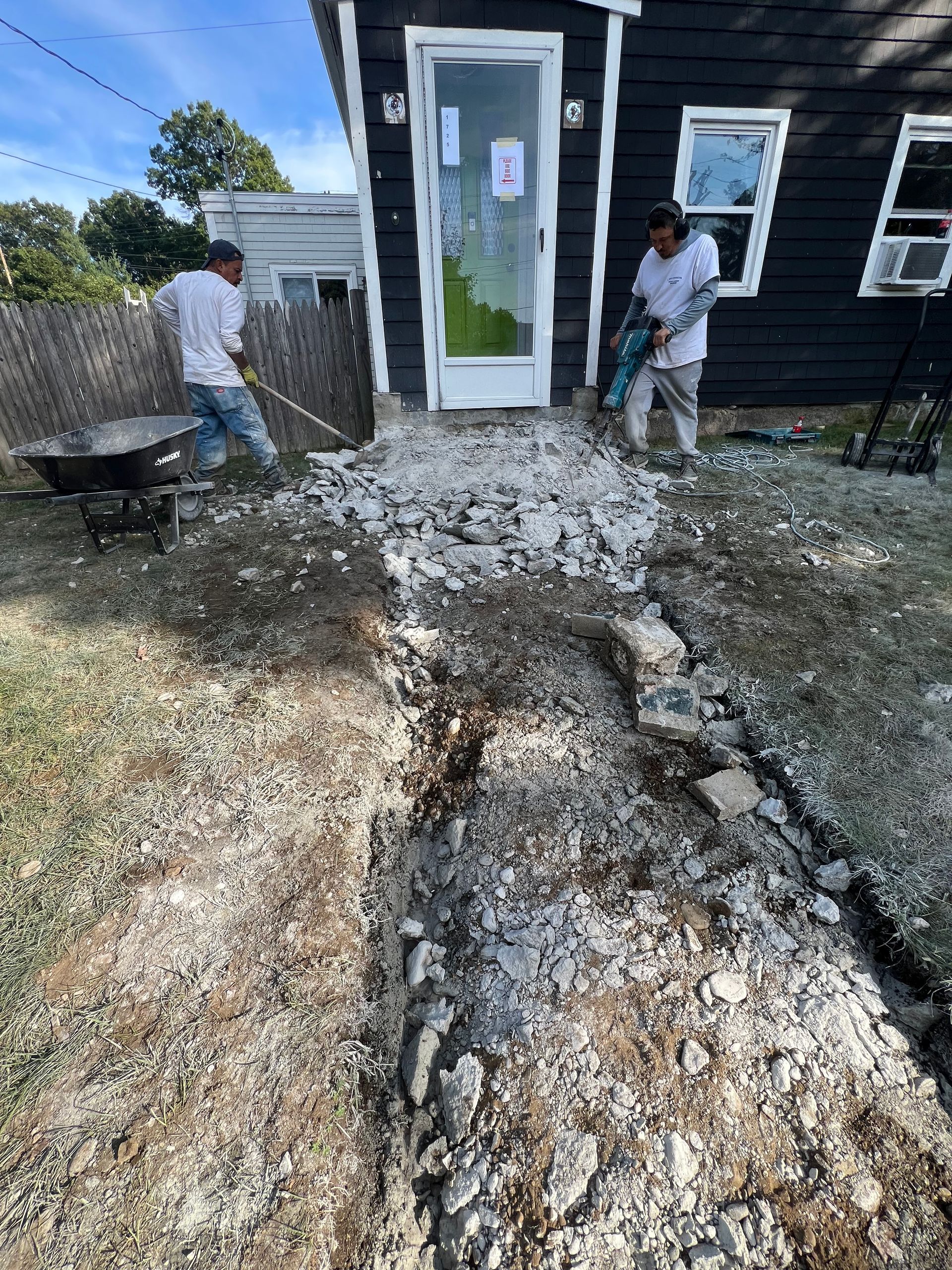 Two workers removing debris in front of a building's back door