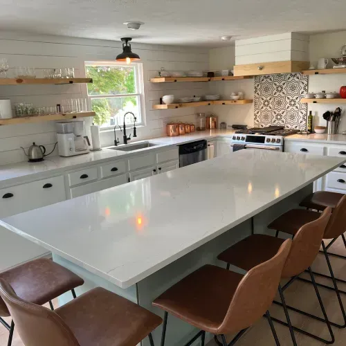 Bright modern kitchen with white island, open shelves, and brown chairs