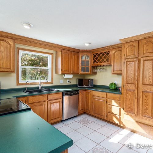Bright kitchen with oak cabinets, green countertops, tiled floor, and a window over the sink.