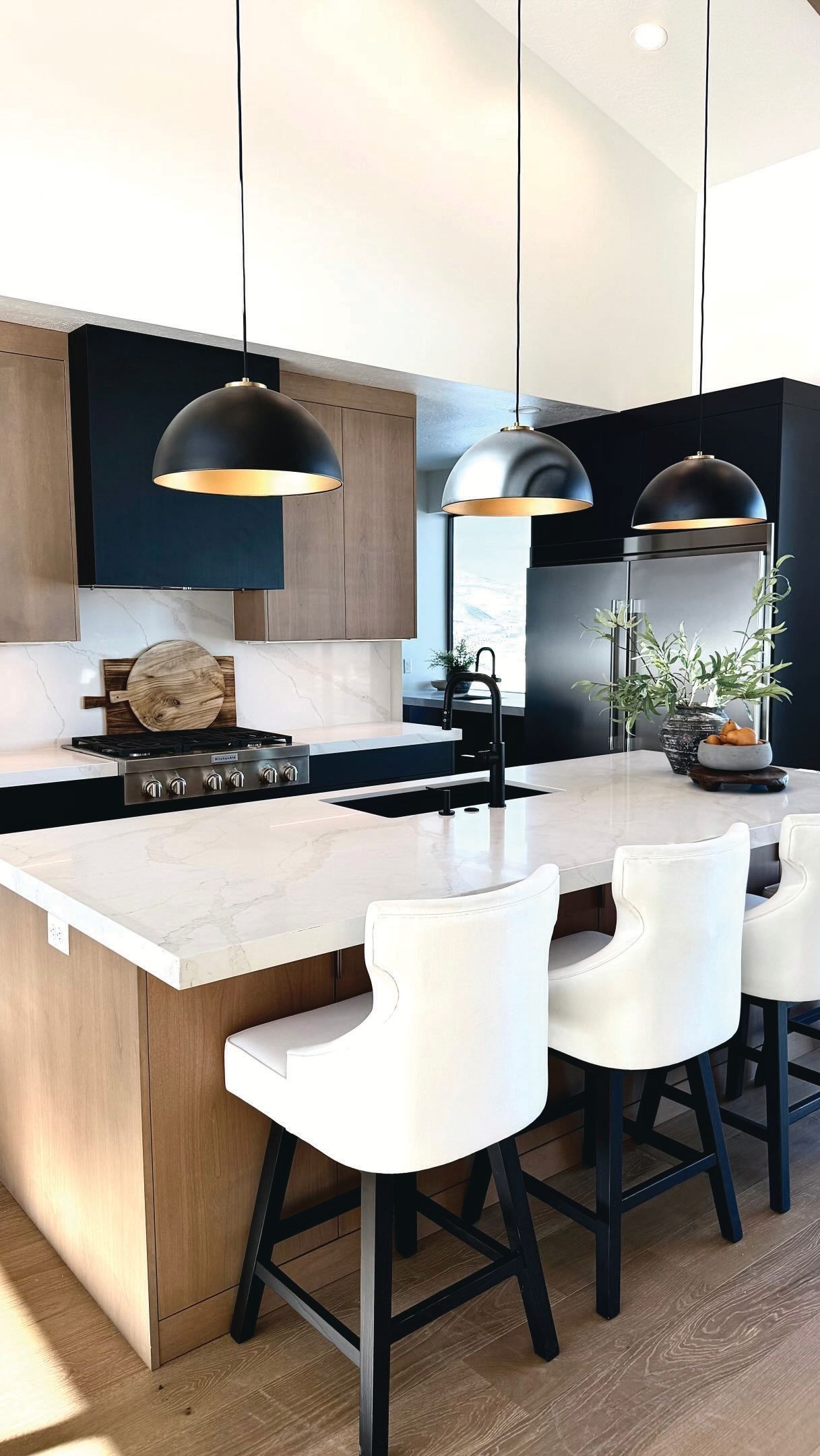 Modern kitchen with white island, black pendant lights, and three white bar stools