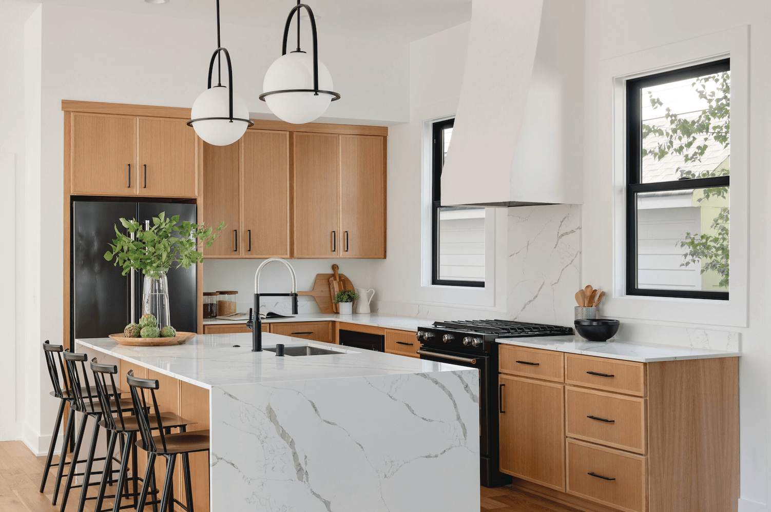 Bright modern kitchen with wood cabinets, marble island, black stools, and pendant lights