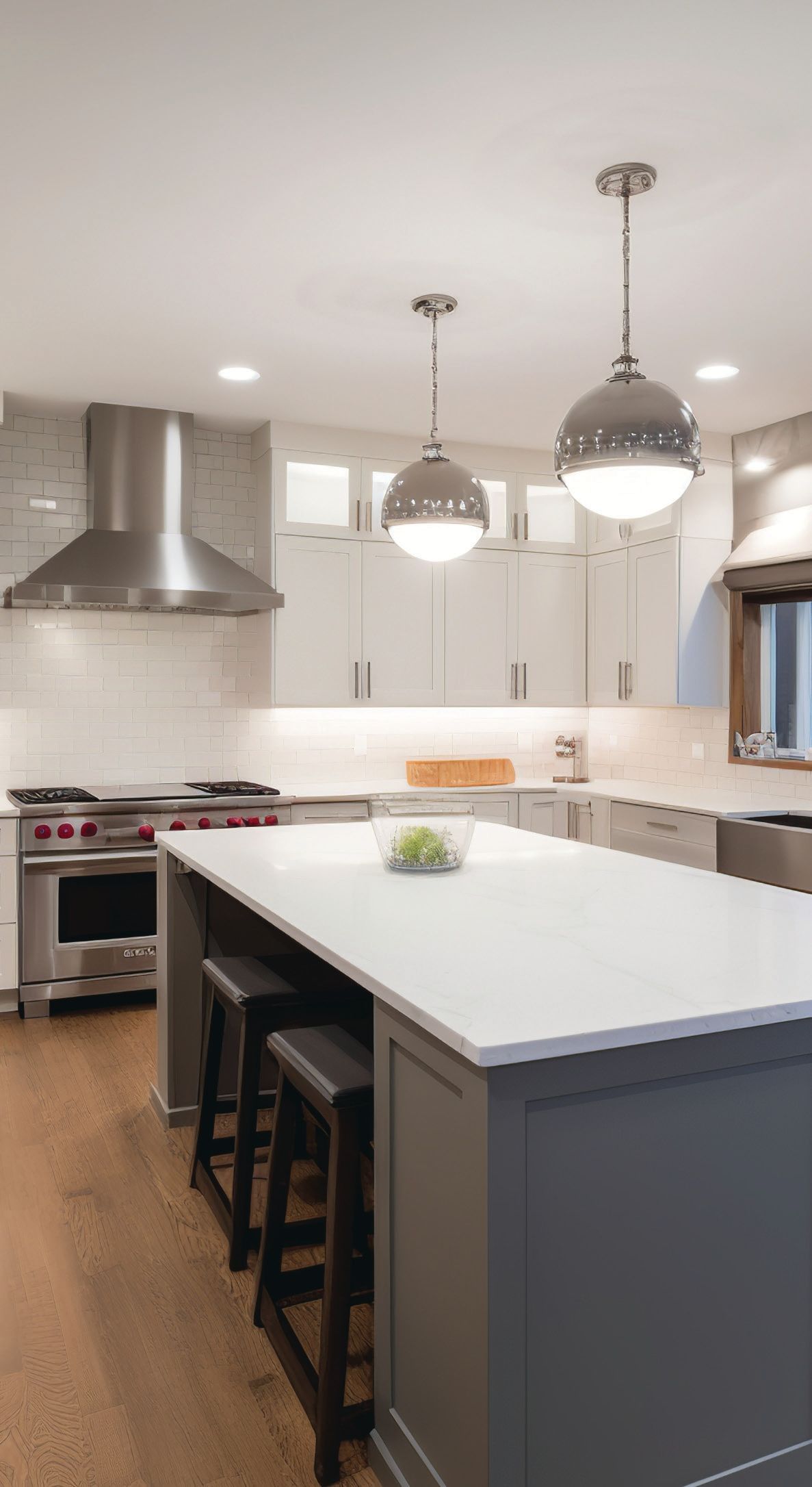 Modern kitchen with large island, pendant lights, stainless steel range hood, and bar stools