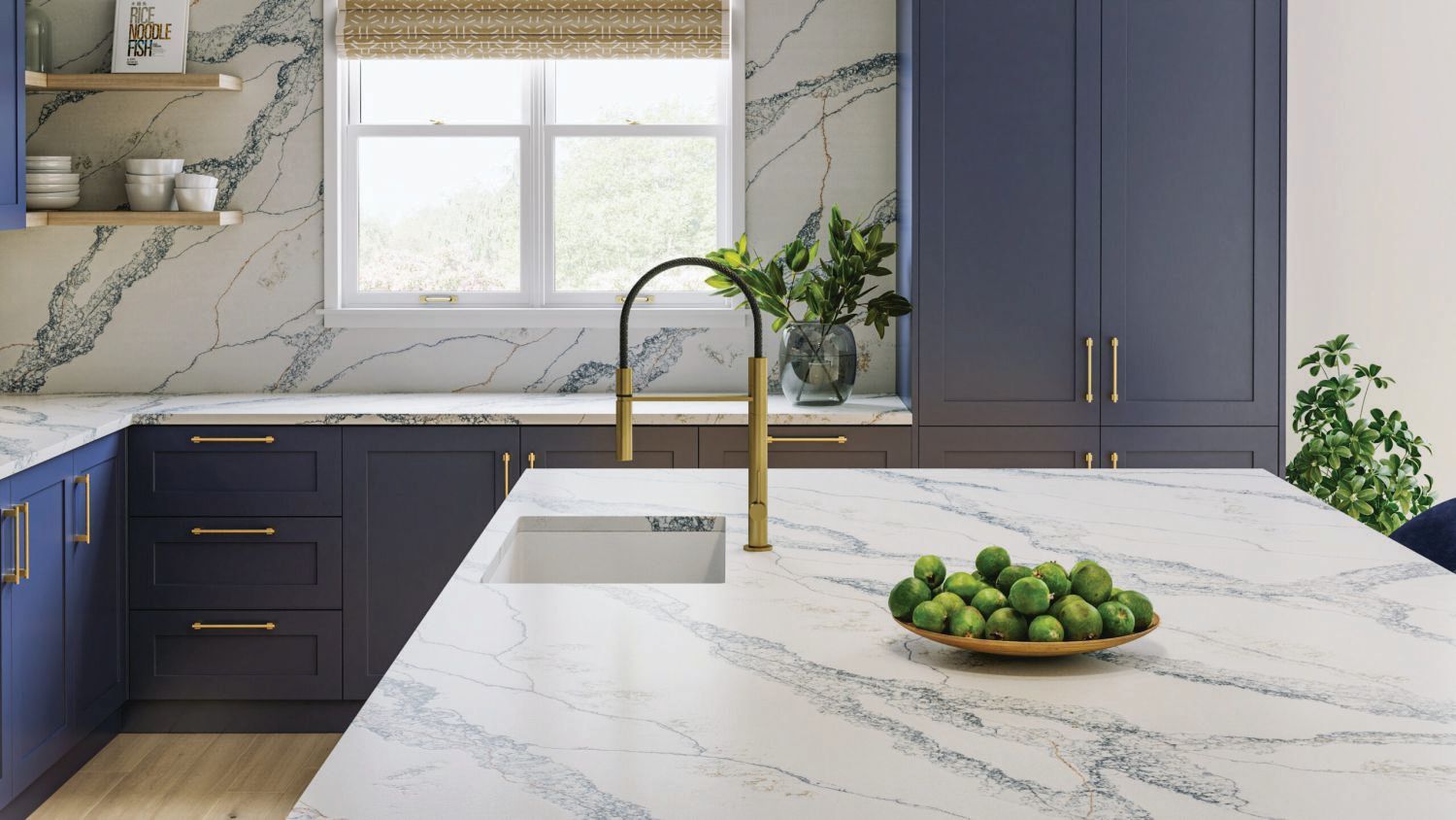 Modern kitchen with navy cabinets, marble island, brass faucet, and a bowl of green fruit by a window