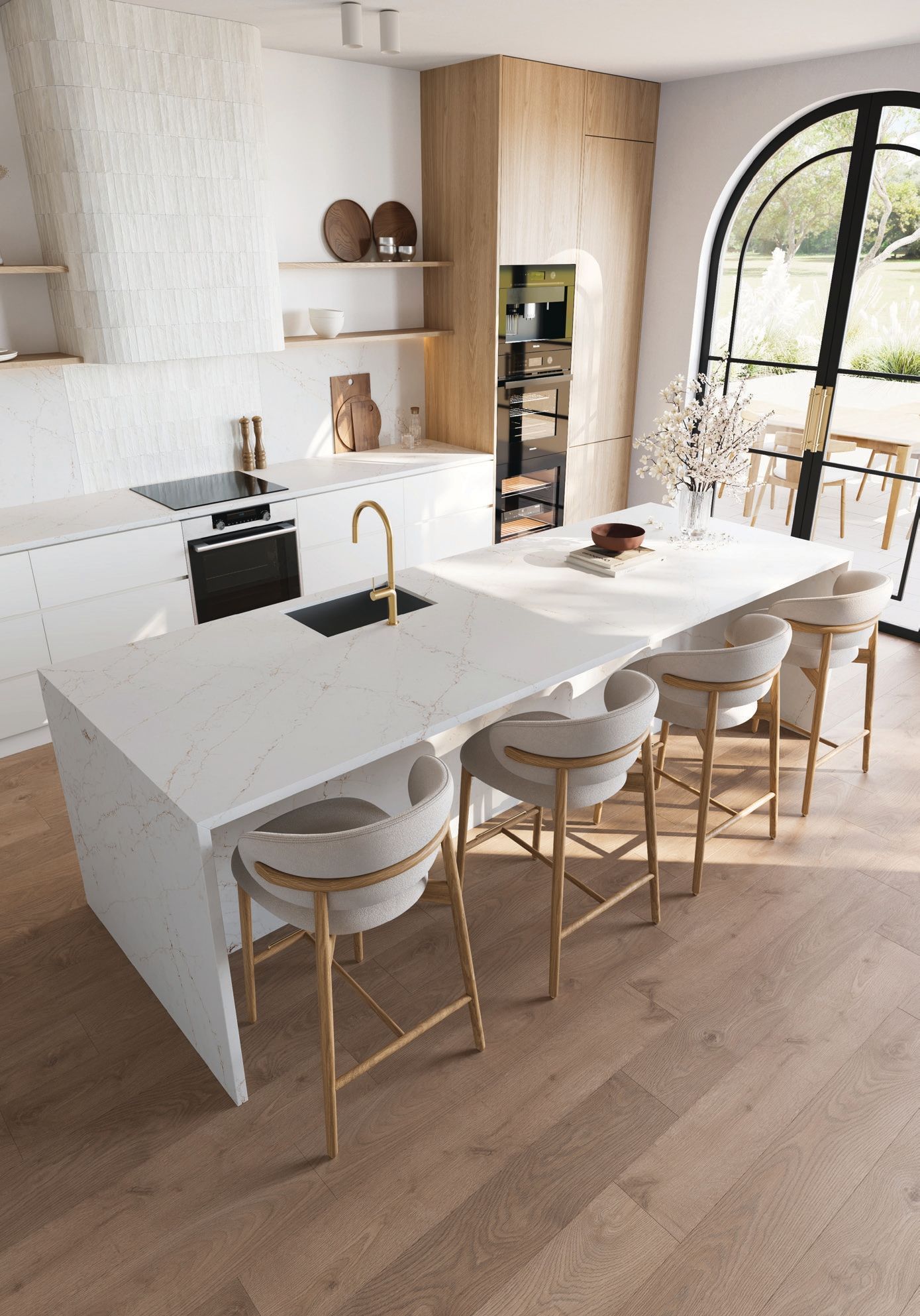 Modern white kitchen with marble island, gold fixtures, and four stools beside a large arched window.
