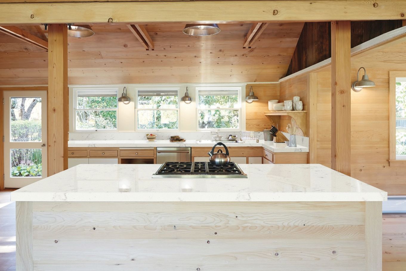 Bright modern kitchen with white island, wooden beams, and windows overlooking greenery