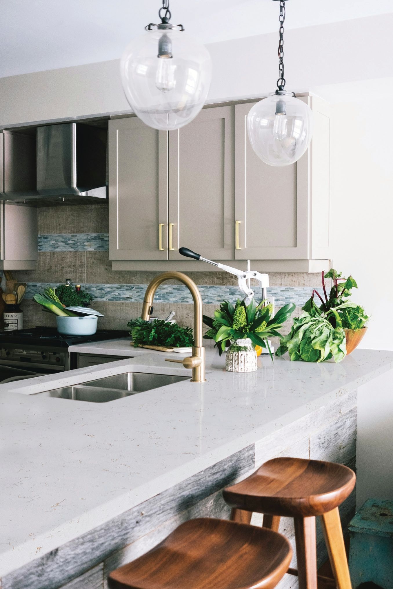 Bright modern kitchen island with pendant lights, sink, plants, and two wooden stools