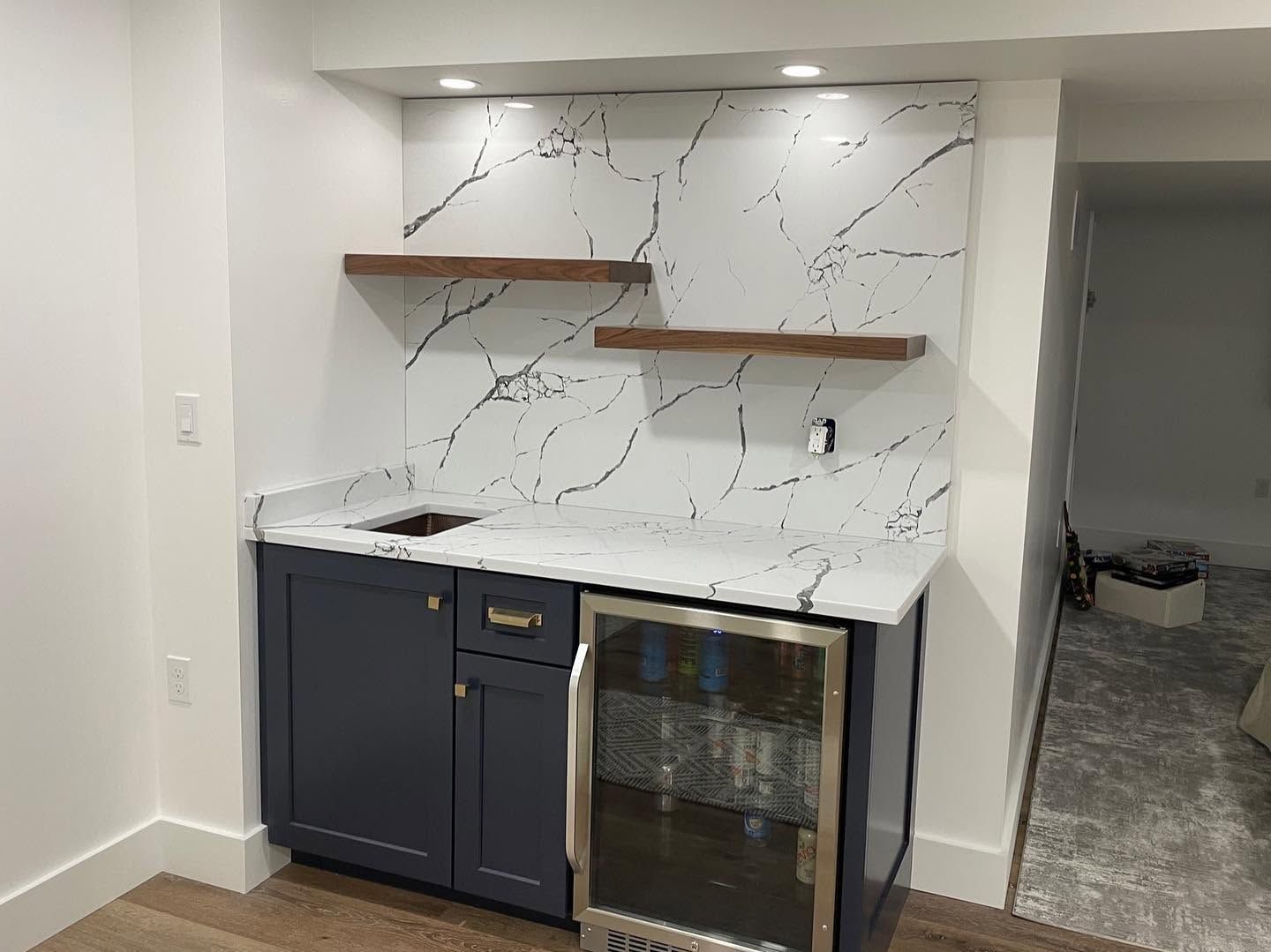 Built-in bar nook with white marble-look backsplash, dark cabinets, and two wooden shelves