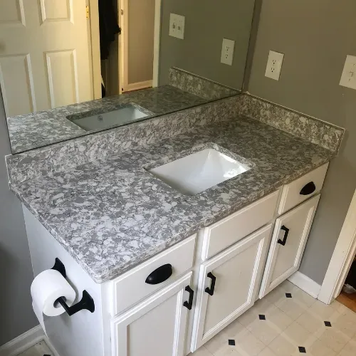 Bathroom vanity with speckled gray countertop, white sink, mirror, and toilet paper holder