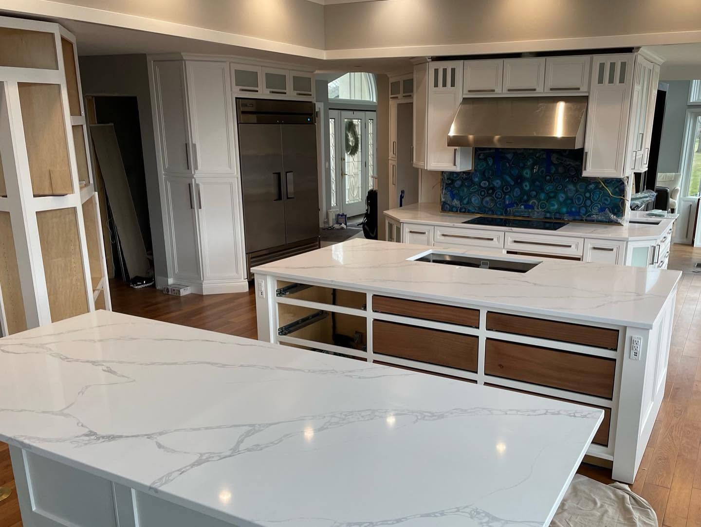 Modern white kitchen with island, glossy countertops, stainless appliances, and blue mosaic backsplash
