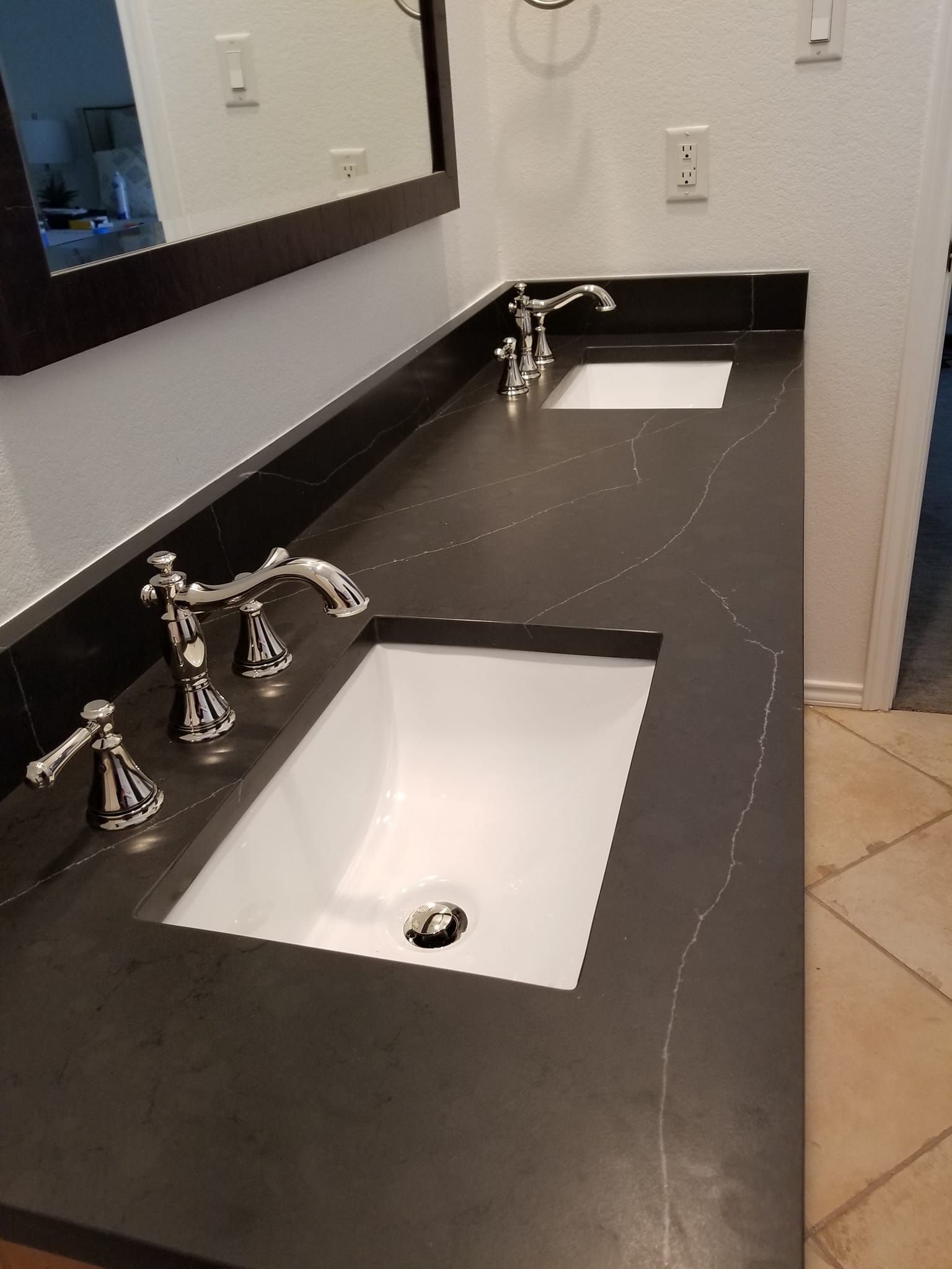 Double sink bathroom vanity with dark countertop, chrome faucets, and wall mirror.