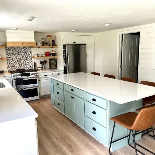 Bright kitchen with mint island, stainless fridge, white cabinets, and wood floors