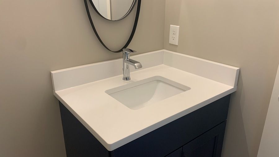 Modern bathroom vanity with white countertop, rectangular sink, and chrome faucet against beige walls.