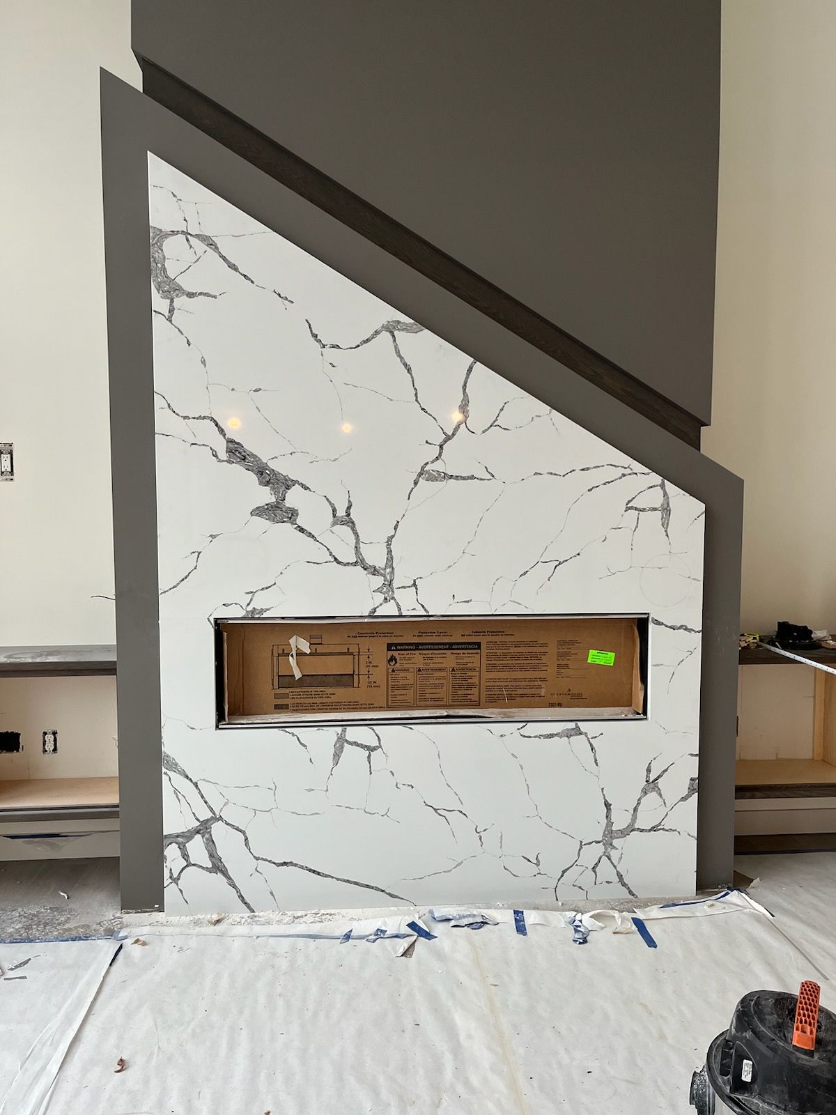 Modern fireplace feature wall with white marble pattern, dark trim, and a recessed firebox opening