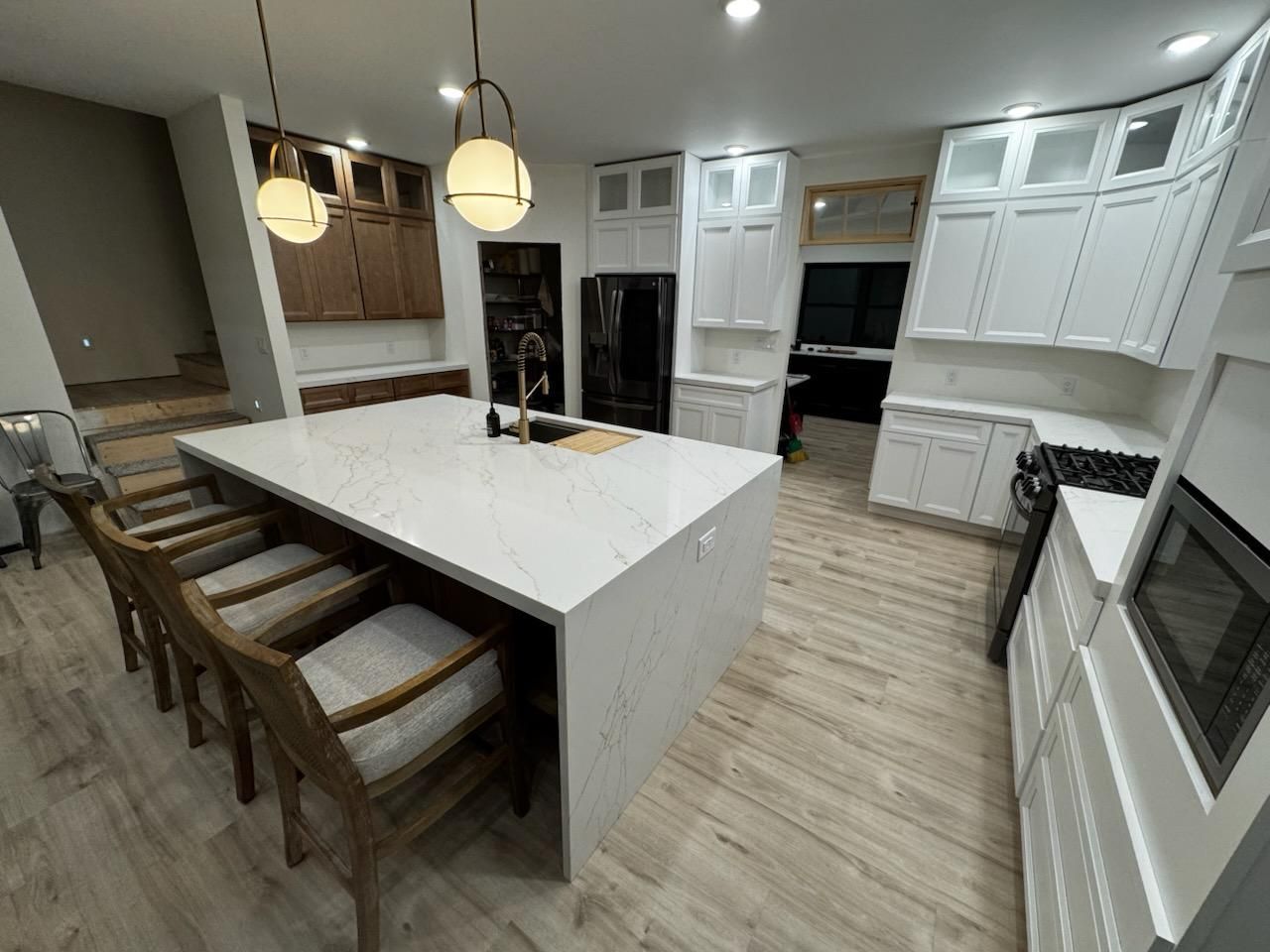 Modern white kitchen with large island, wood flooring, pendant lights, and built-in appliances.