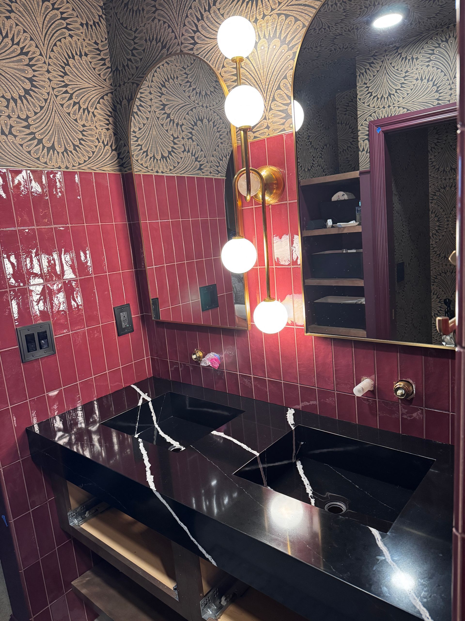 Modern bathroom vanity with black counters, red textured walls, and round illuminated mirror bulbs.