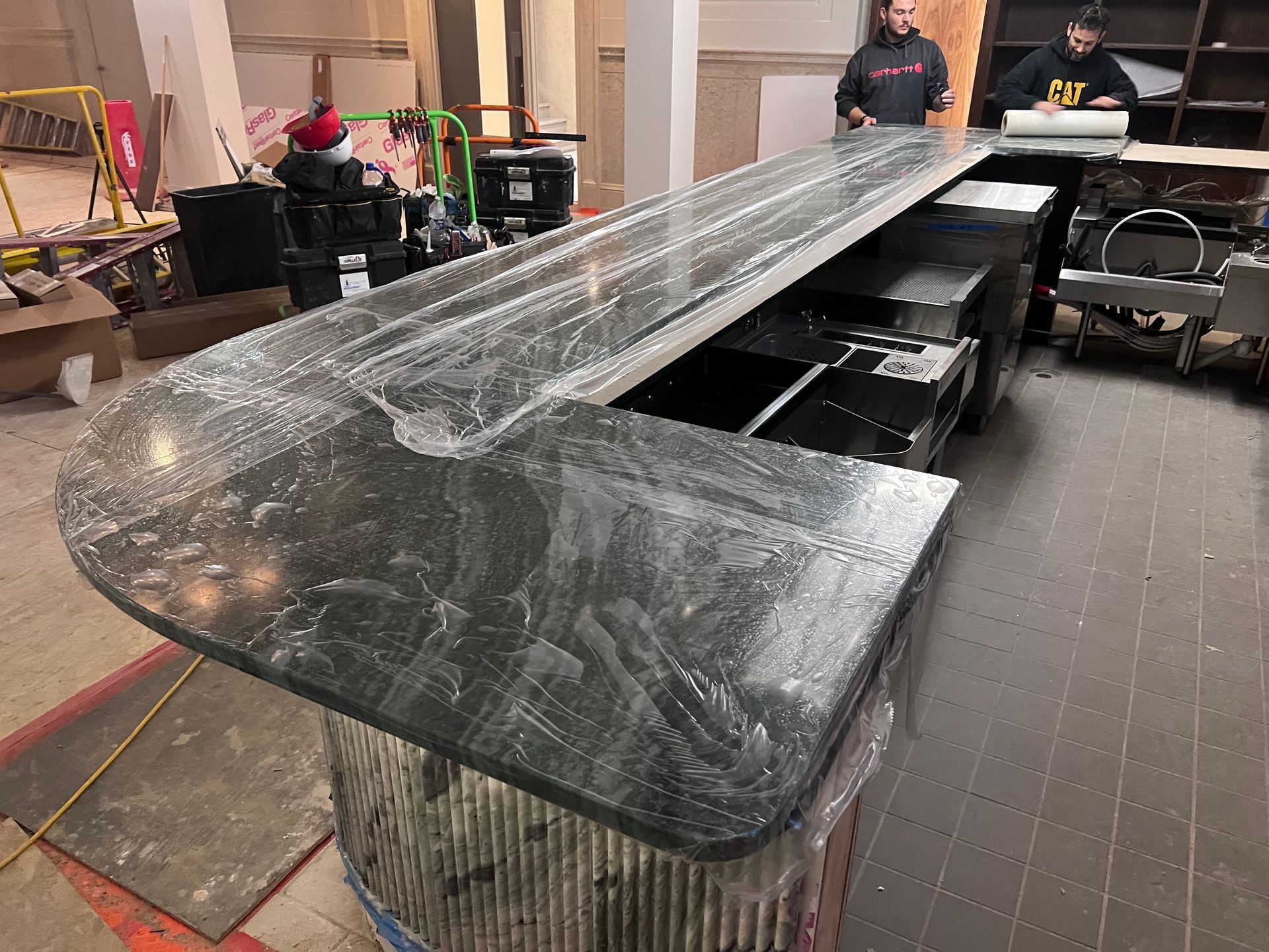 Glossy black grand piano being restored in a workshop, with two people working in the background