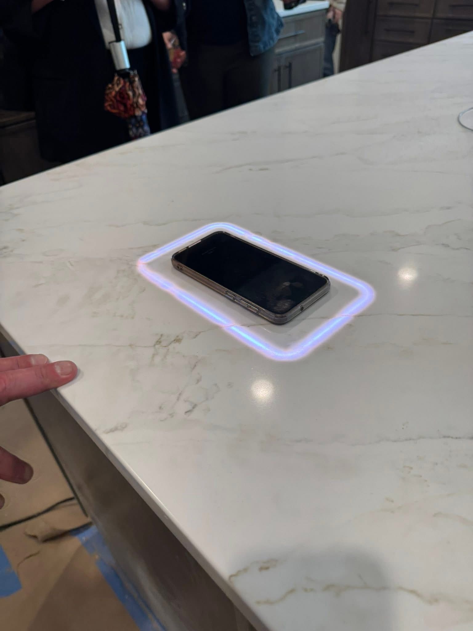 Smartphone lying on a lit wireless charging pad on a white marble countertop.