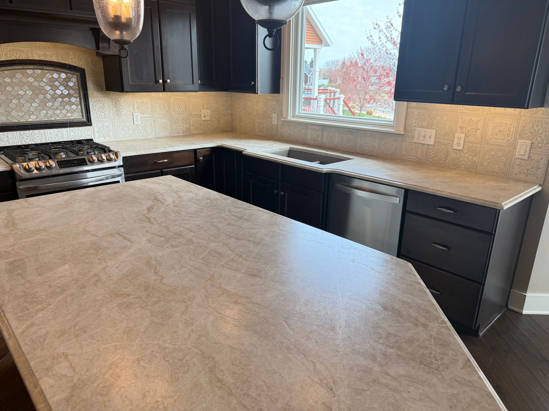Modern kitchen with black cabinets, beige countertops, gas stove, dishwasher, and window over the sink