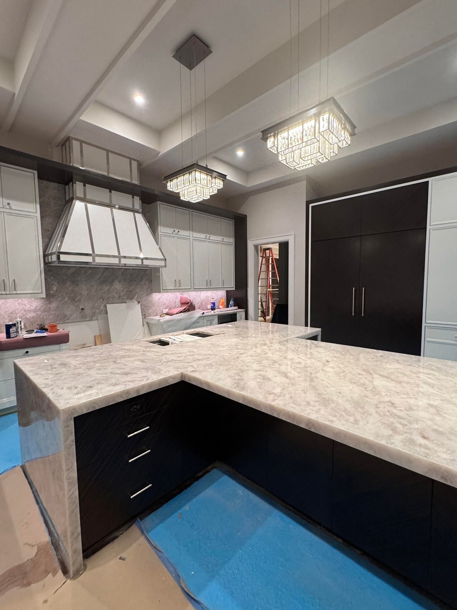 Modern kitchen with black cabinets, marble island, crystal pendant lights, and blue floor matning