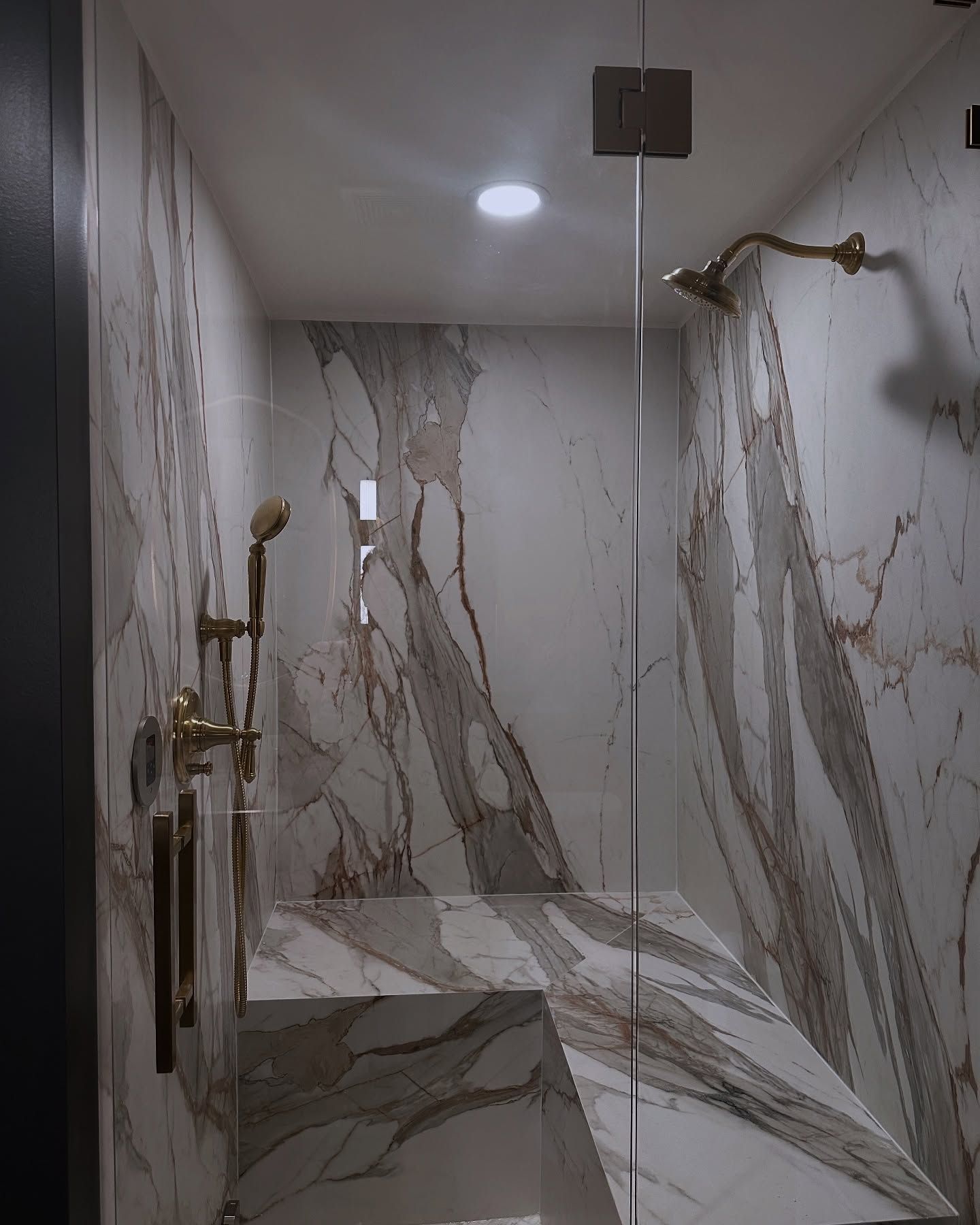 Marble-tiled shower with glass partition, brass fixtures, and a rainfall showerhead