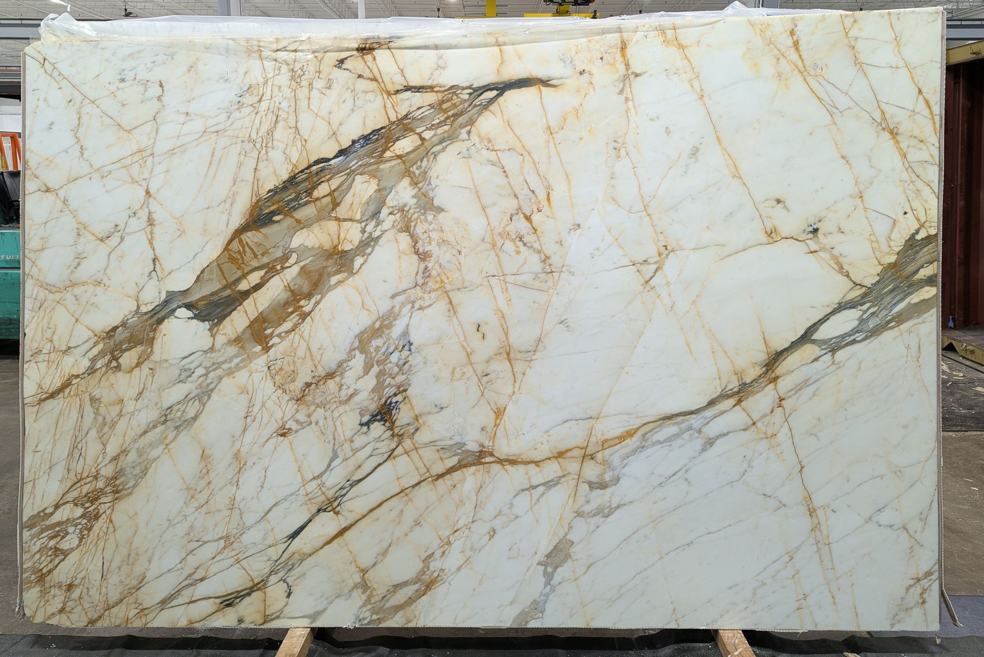 Large polished white marble slab with gold and gray veining on a display stand.