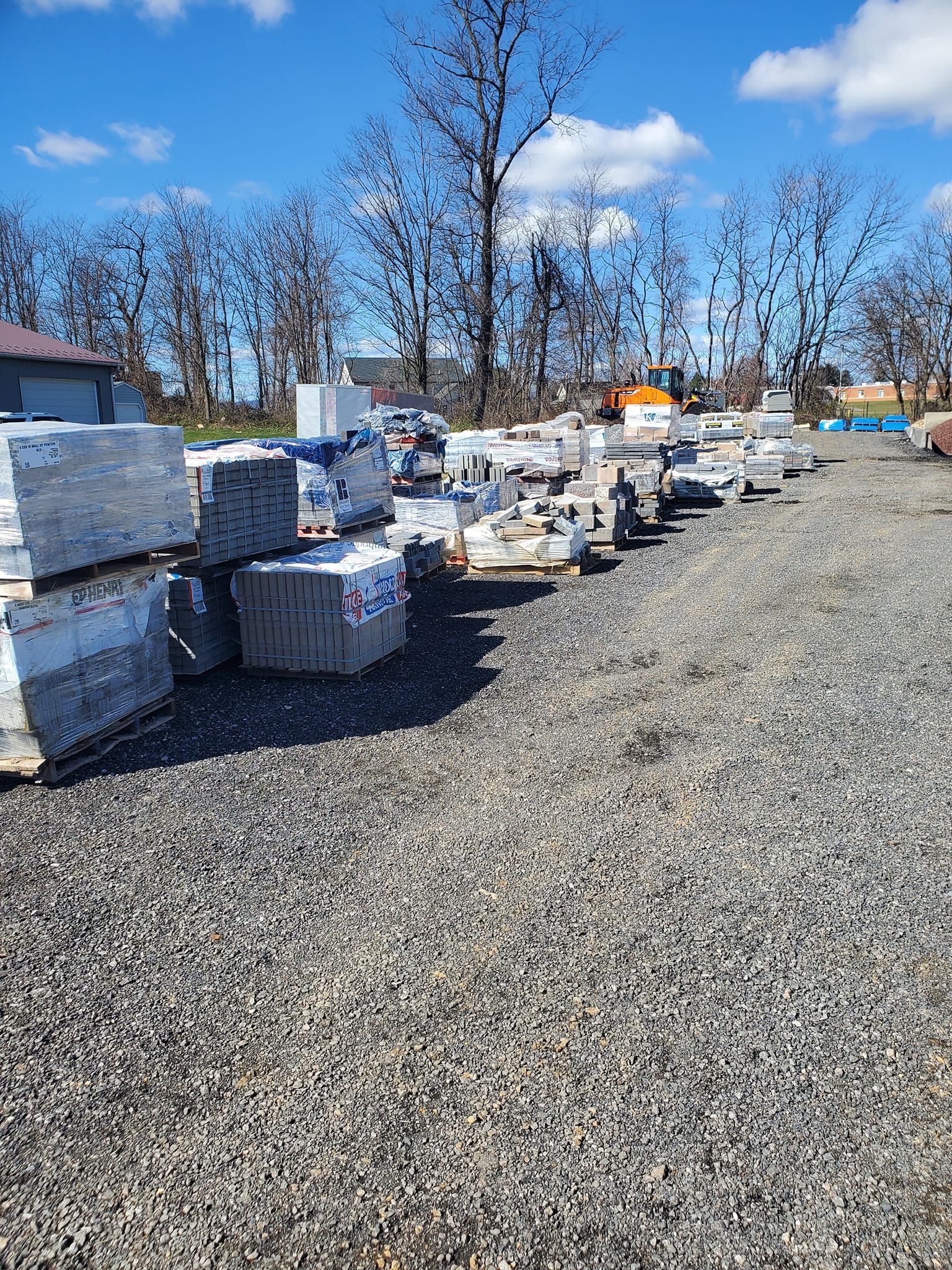 A lot of bricks are stacked on top of each other in a gravel lot.