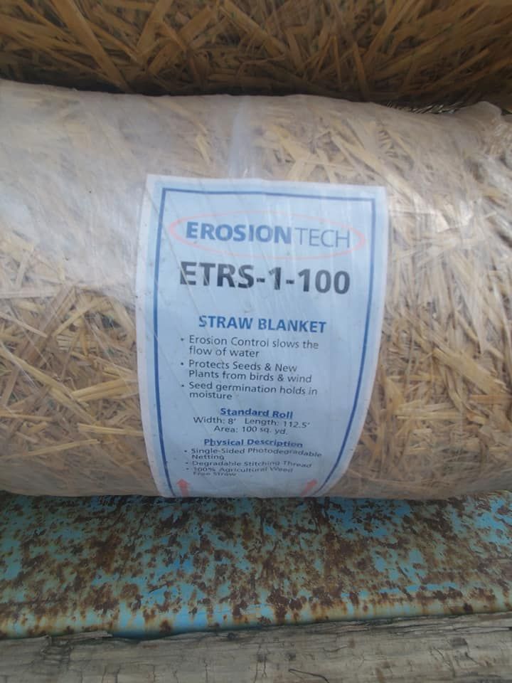 A roll of straw blanket with a label on it is sitting on top of a wooden table.