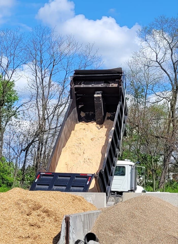 A dump truck is dumping sand into a pile of gravel.