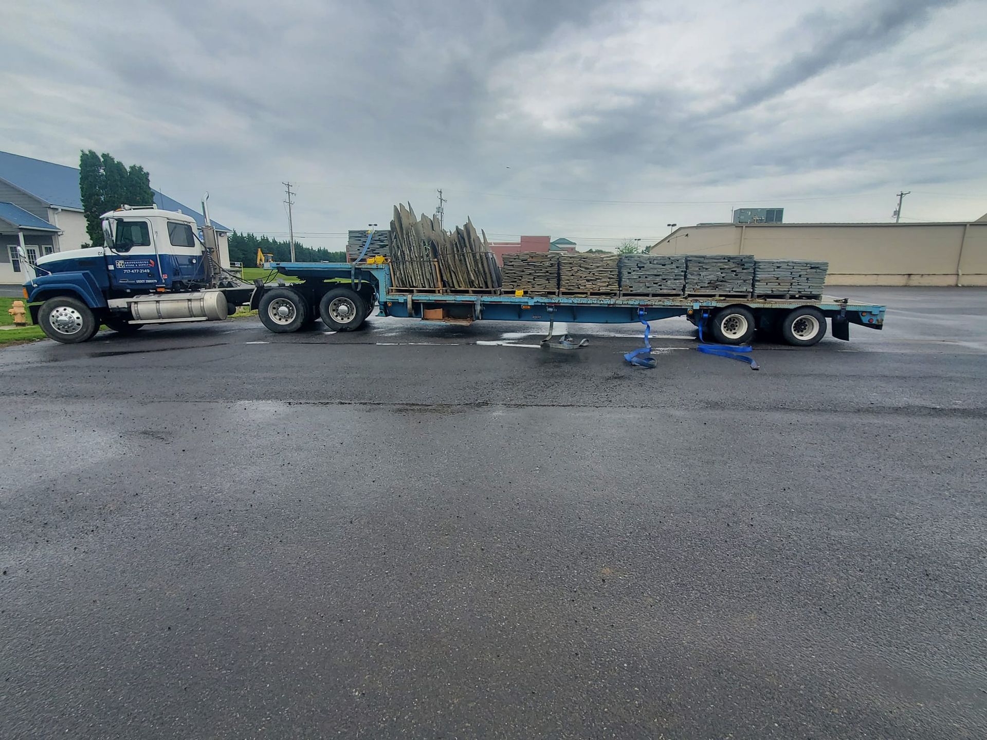 A blue semi truck is pulling a trailer full of rocks.