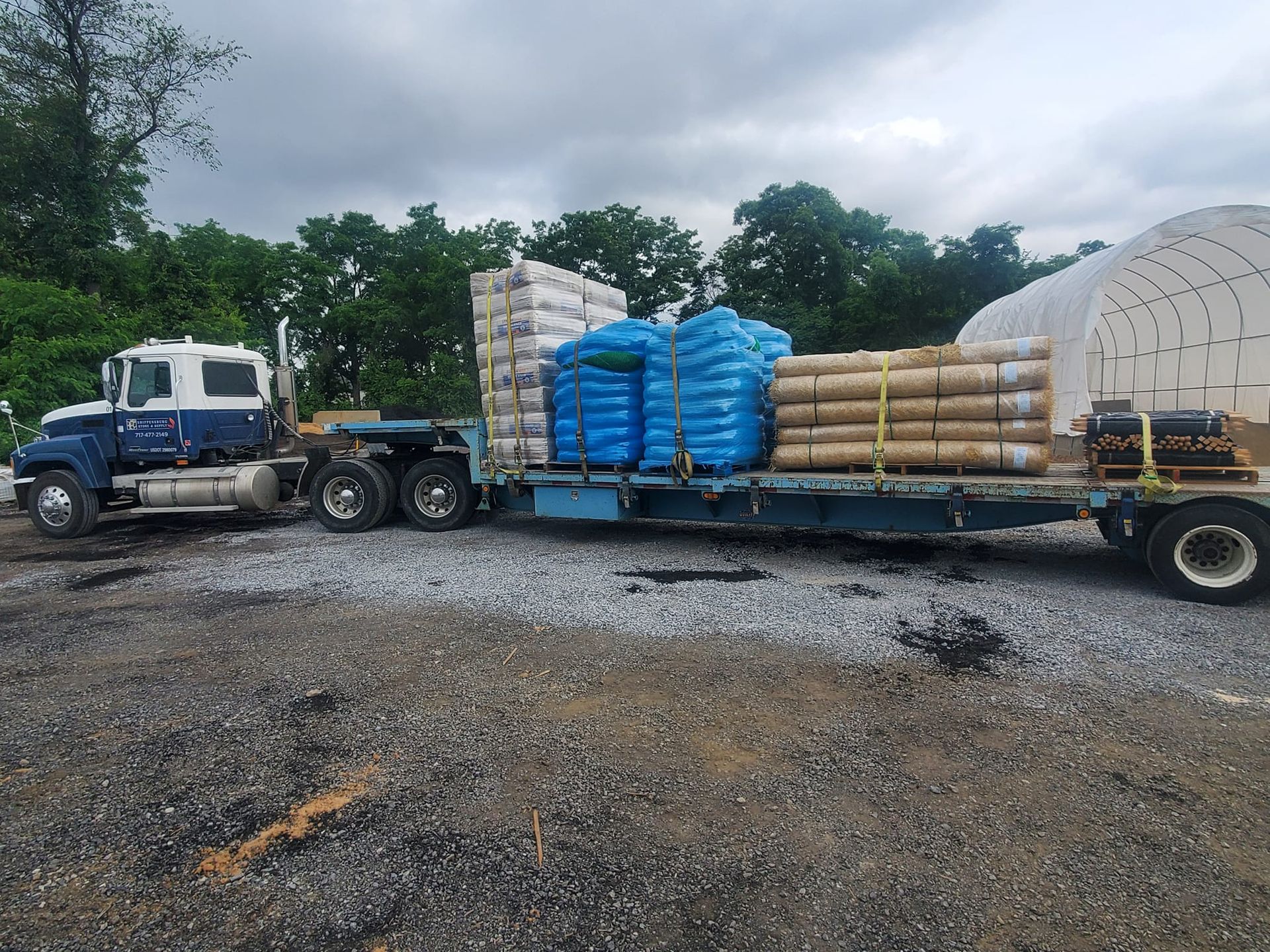 A semi truck is carrying a trailer filled with bags of wood.