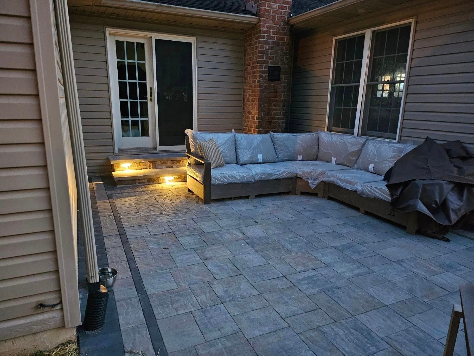 A patio with a sectional couch and a grill in front of a house.
