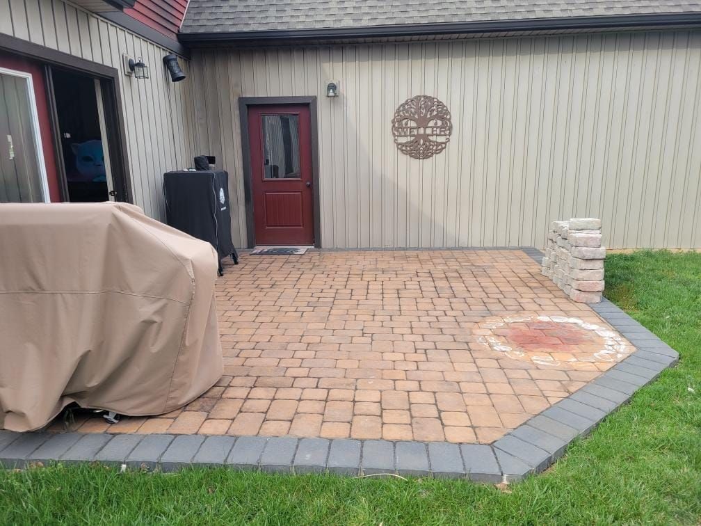 A brick patio with a grill on it in front of a house.