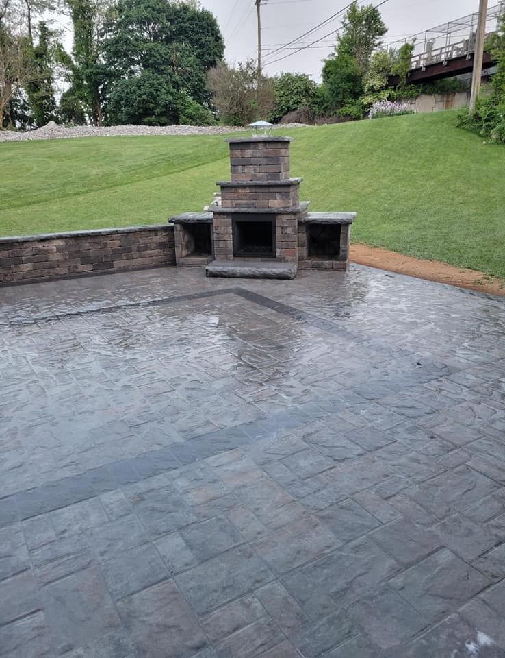 A brick fireplace is sitting on top of a patio next to a lush green field.