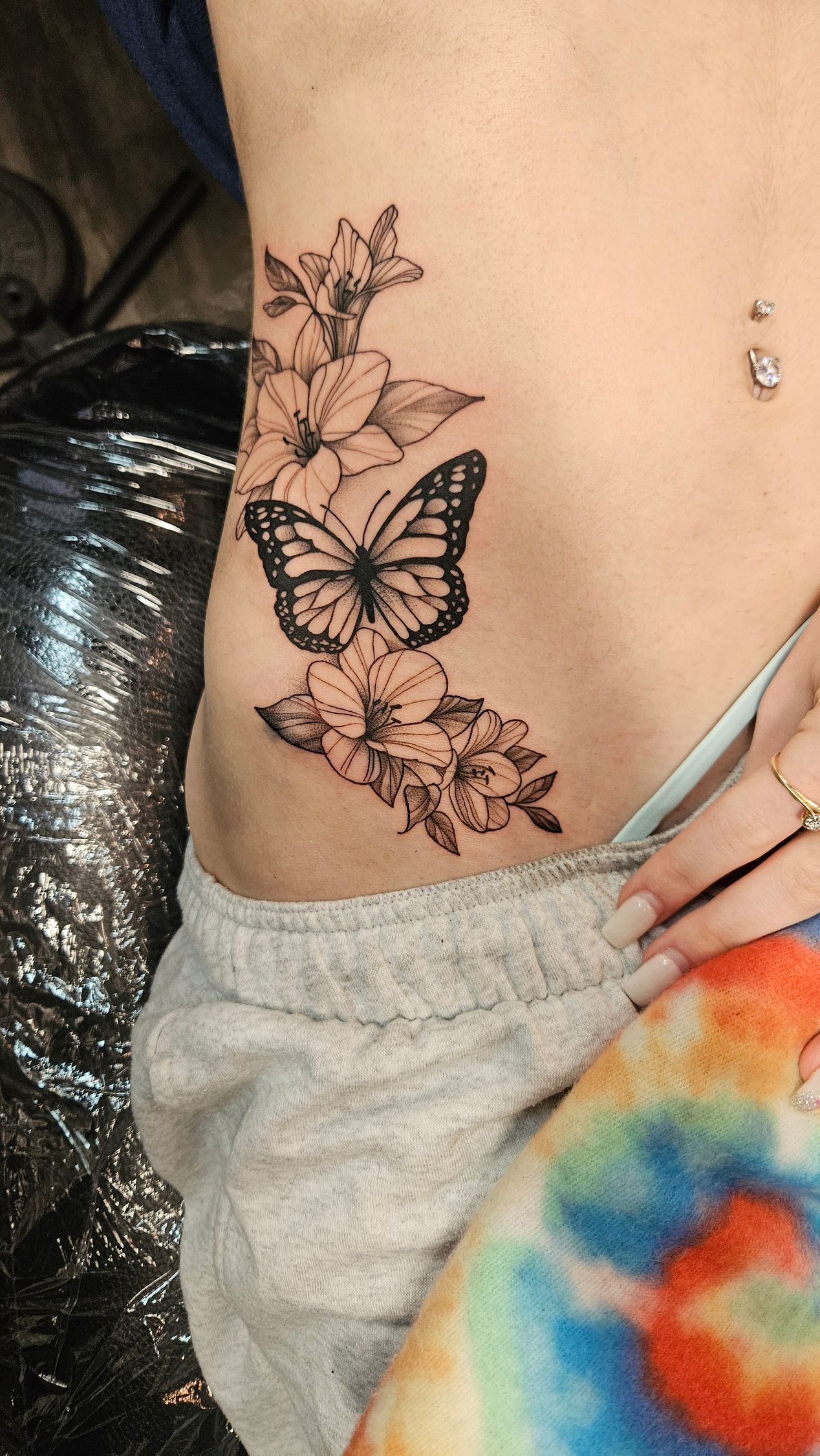 Delicate black butterfly and floral tattoo on a person’s side near the waist.