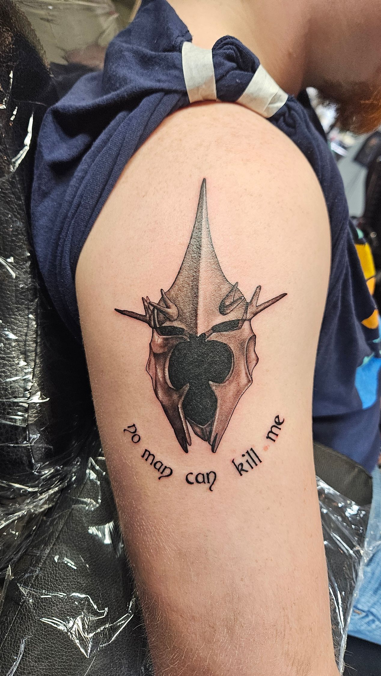 Close-up of an upper arm with a small black tattoo of a dagger or compass design