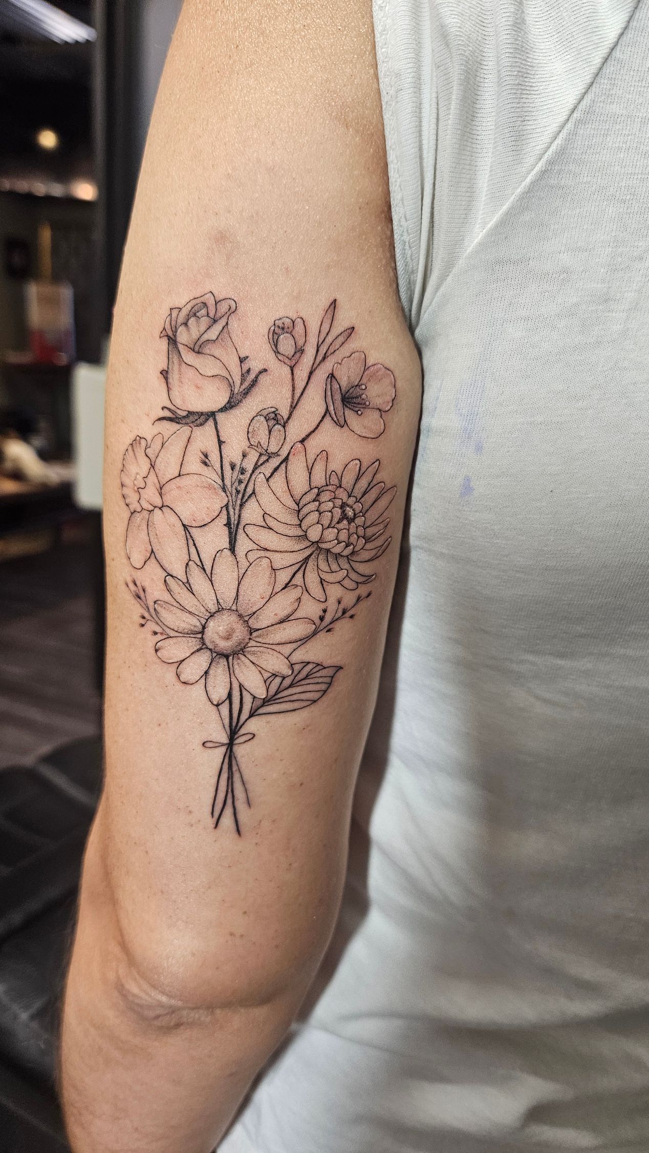 Close-up of an upper arm with a delicate black floral line-art tattoo.