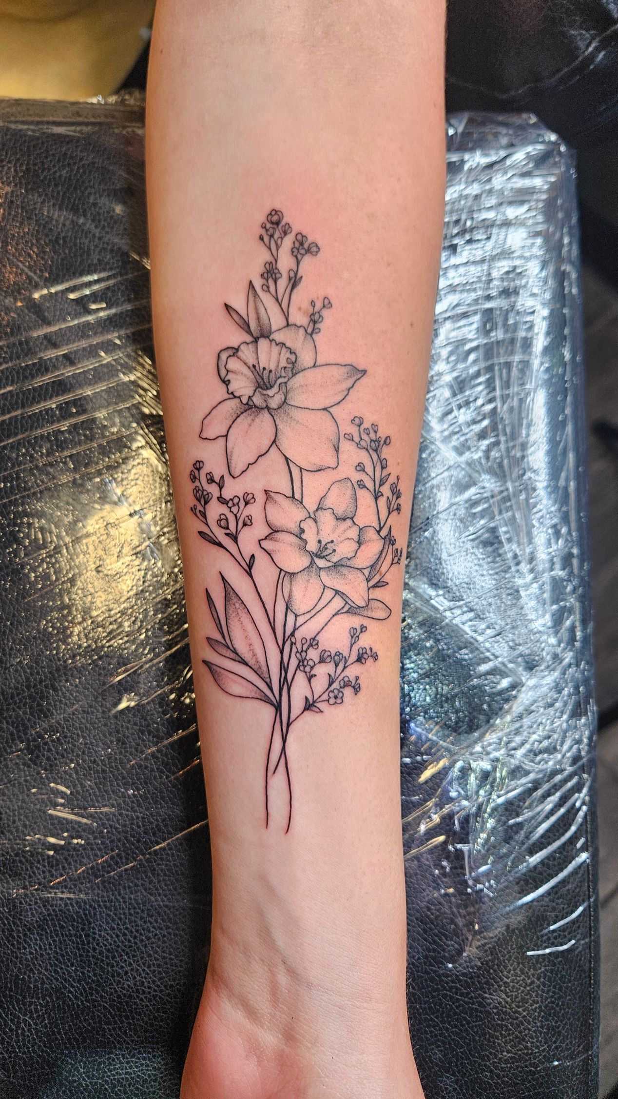 Black floral tattoo on a forearm, featuring delicate flowers and stems on skin.