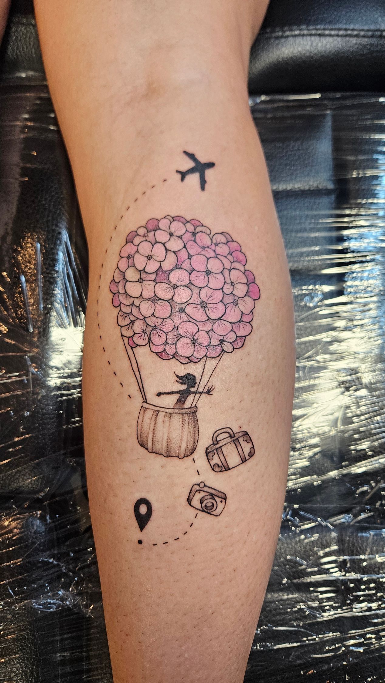 Leg tattoo with purple flower, small airplane, and tiny black travel-themed symbols