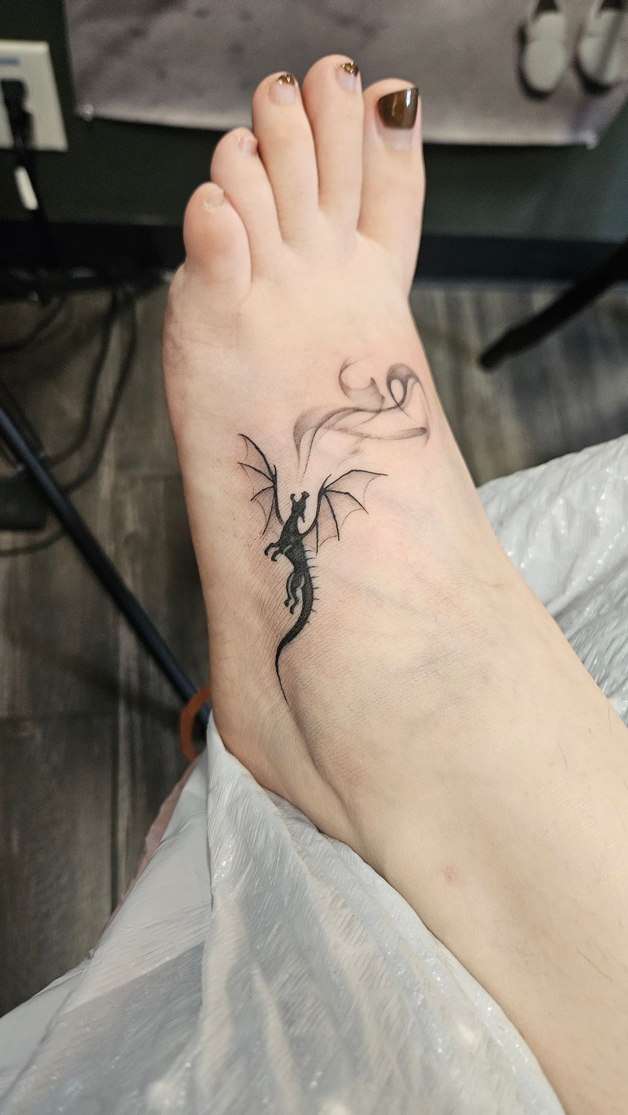 Bare foot and ankle with black tattoos, resting on a chair.