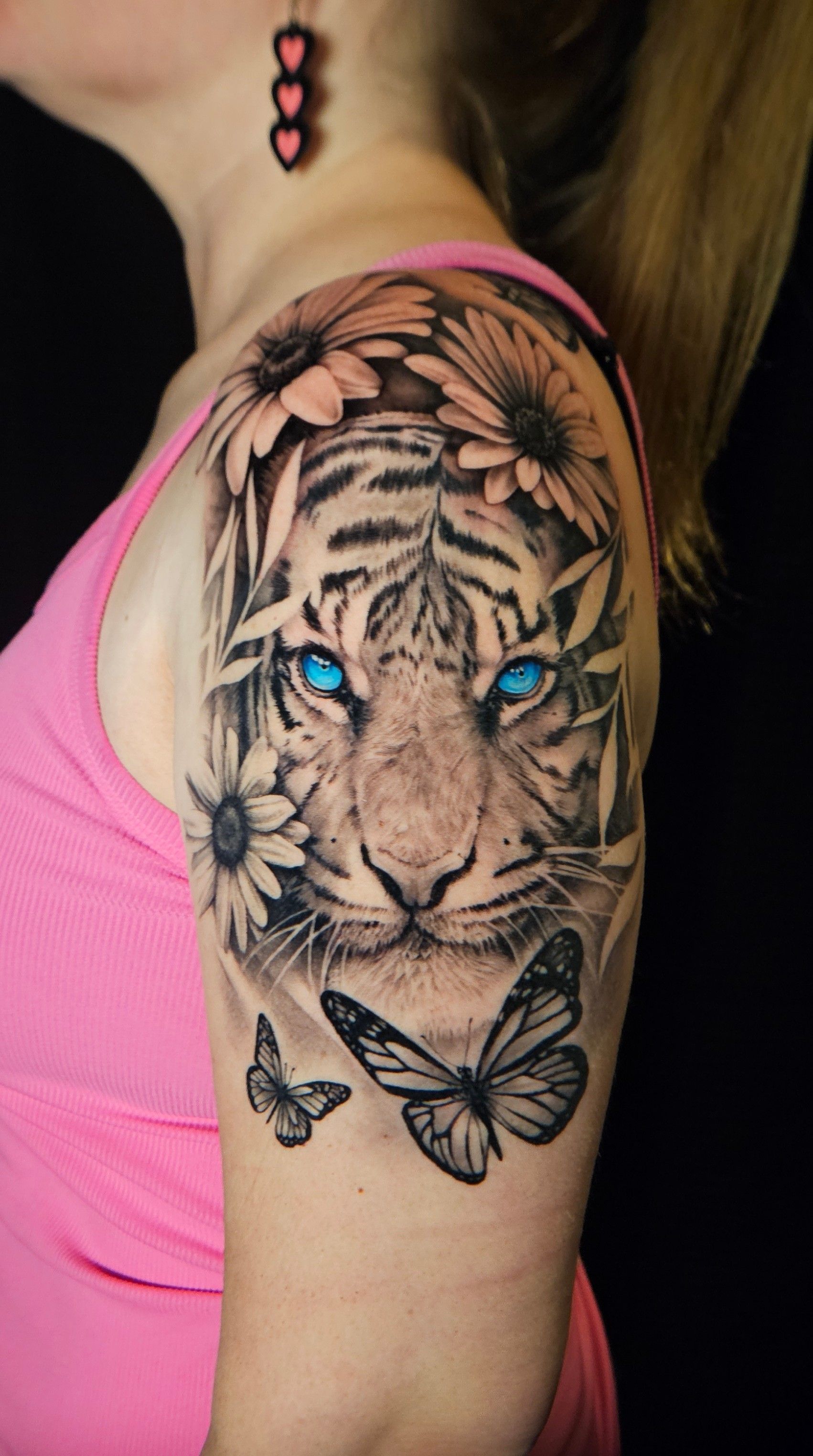 Tattooed tiger with blue eyes and butterflies on a woman’s upper arm, wearing a pink top