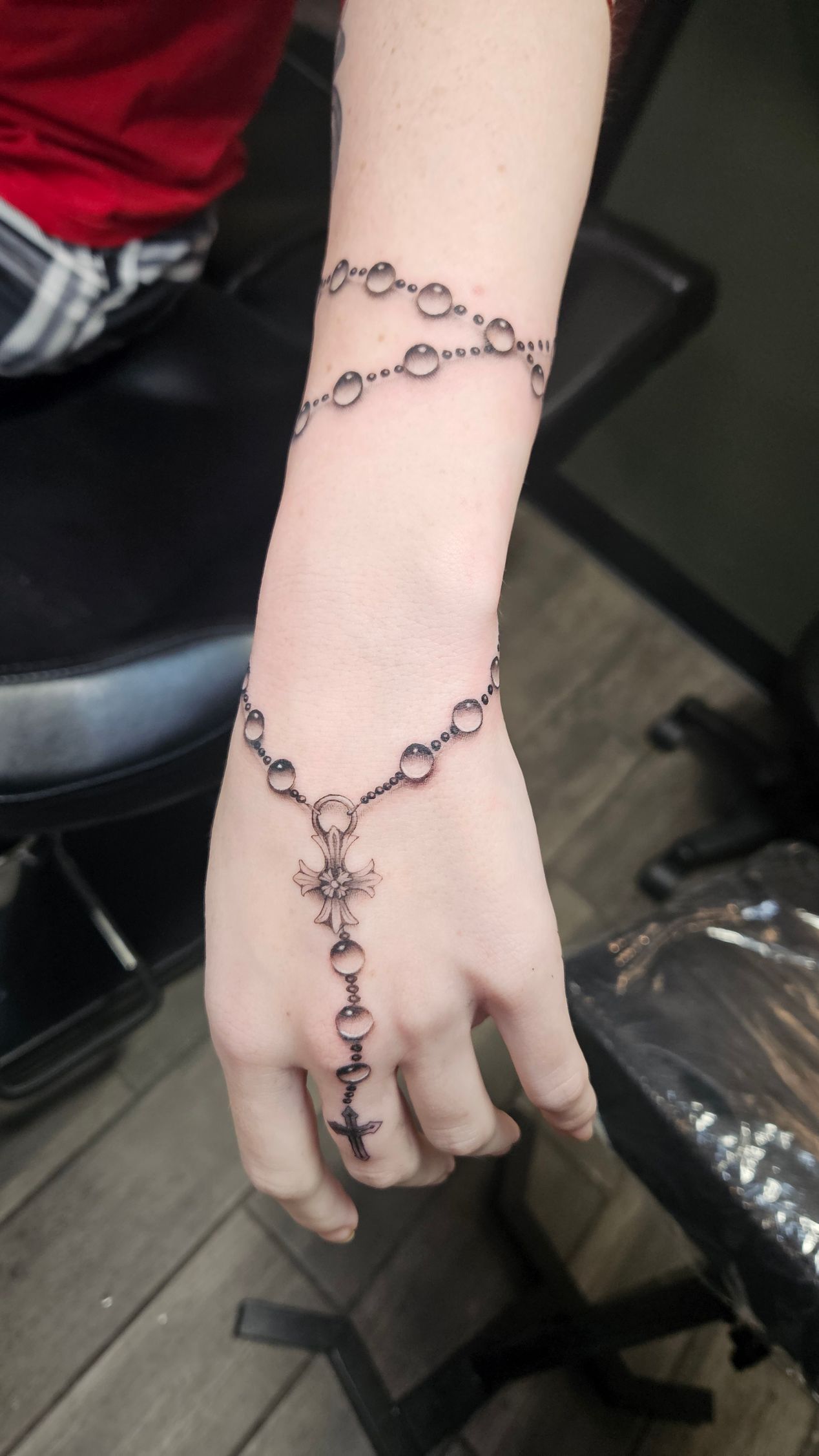 Arm with black chain jewelry draped from wrist to hand over a light gray sleeve