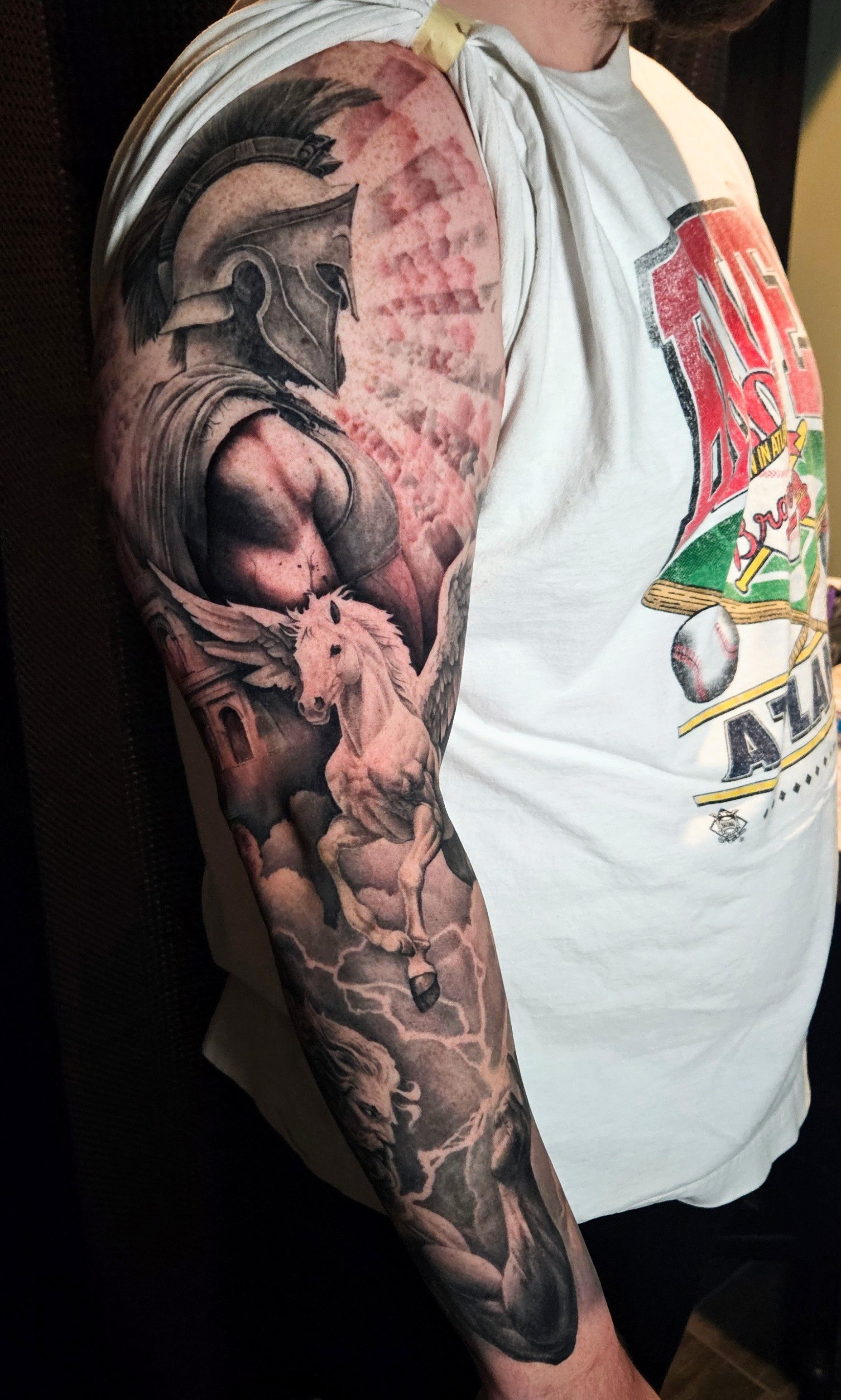 Arm with detailed black-and-gray tattoo sleeve beside a white T-shirt.